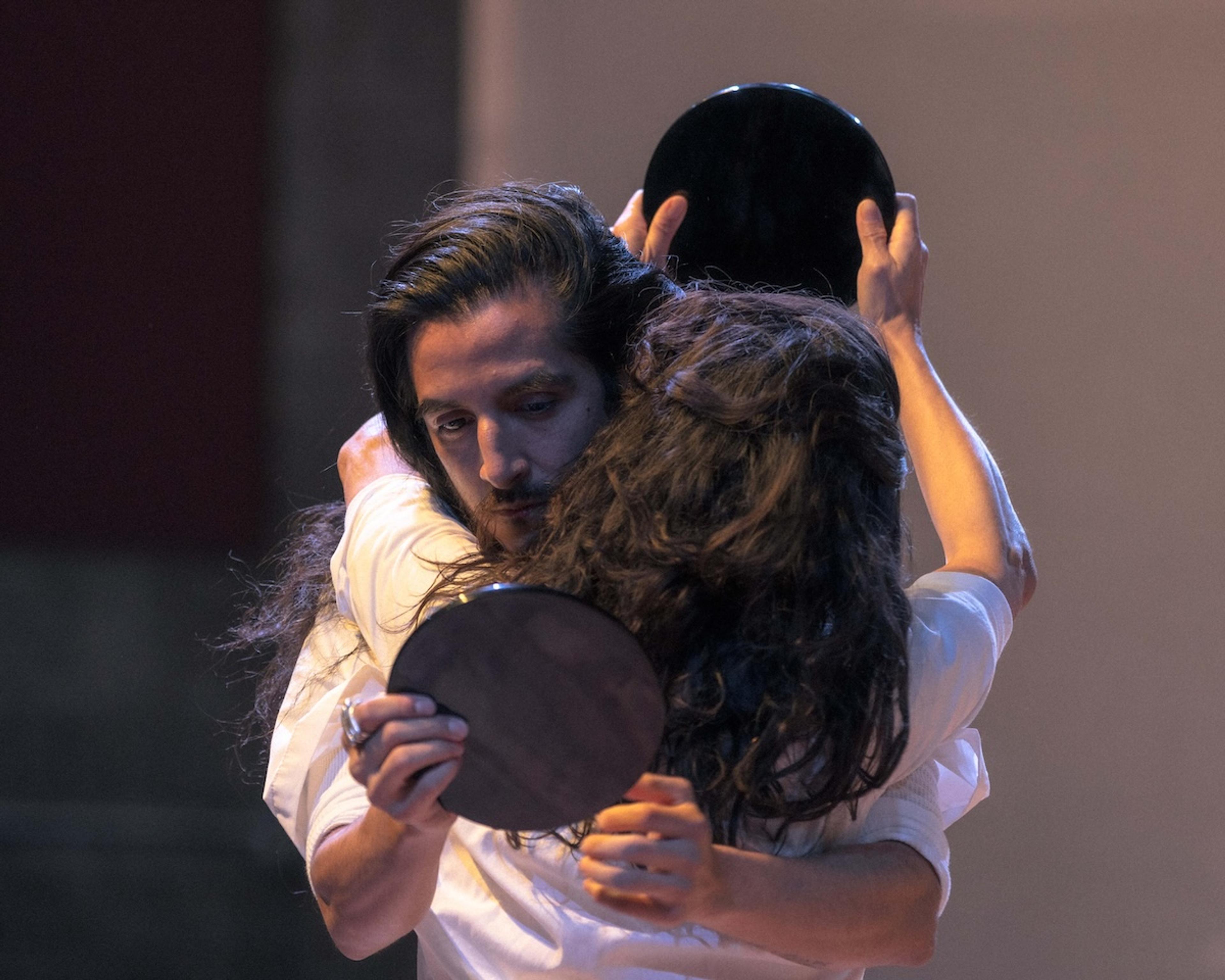 Photo of a couple embracing, each holding a circular mirror, with intense expressions, capturing a moment of connection.