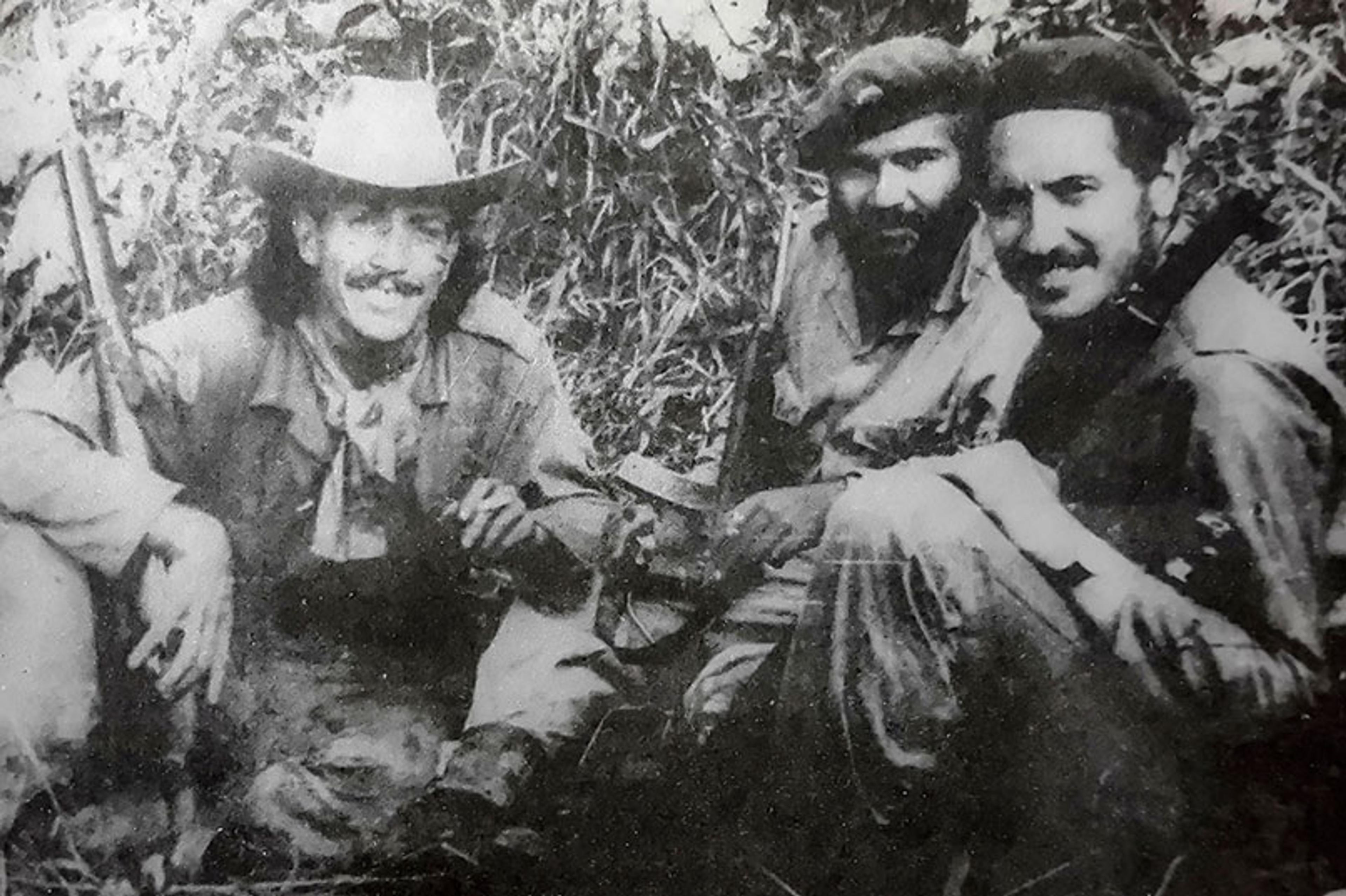 Black and white photo of three men in military attire sitting on grass, holding guns.