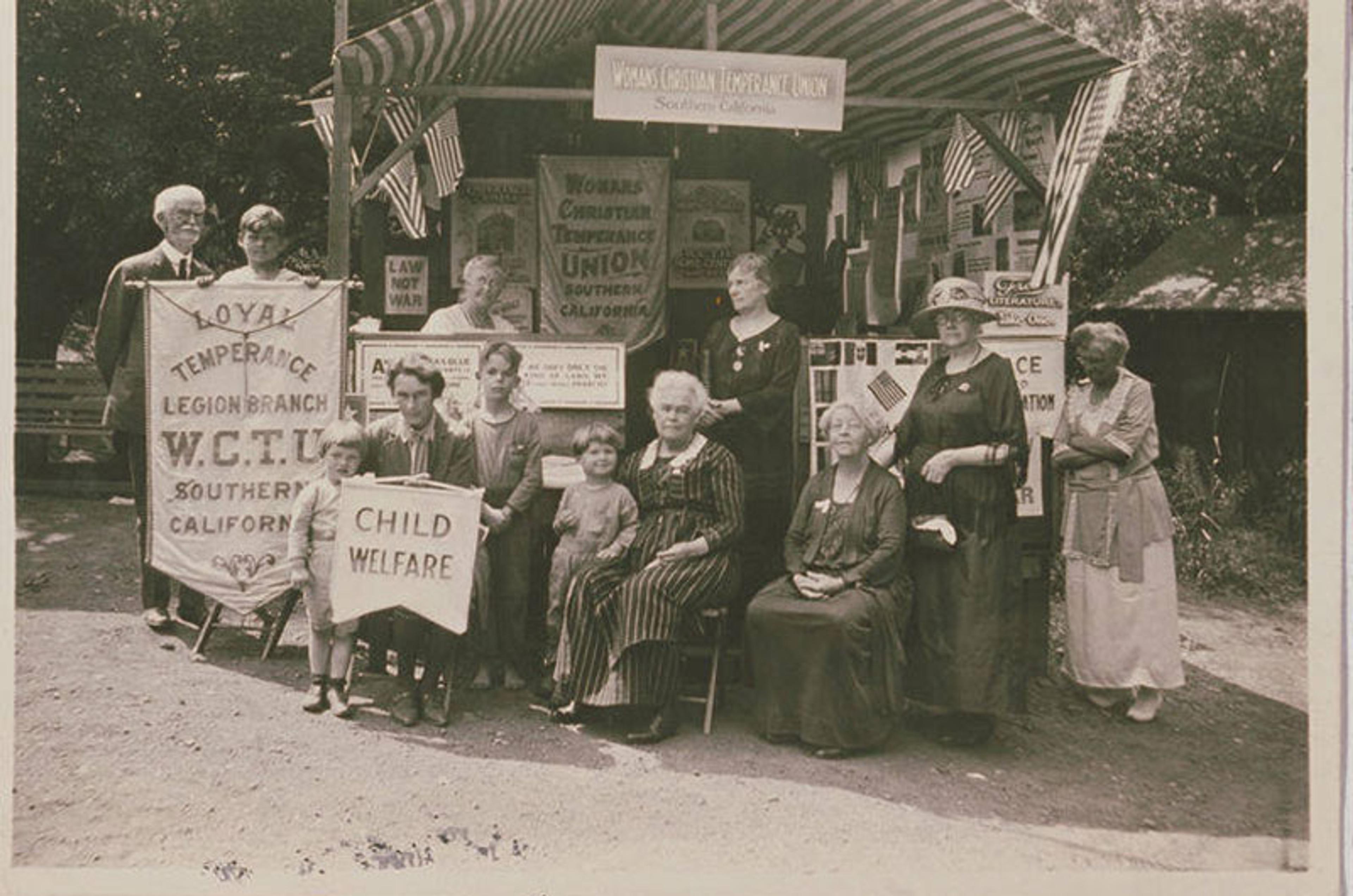 Black-and-white photo of people in front of a Women’s Christian Temperance Union booth with signs about child welfare.