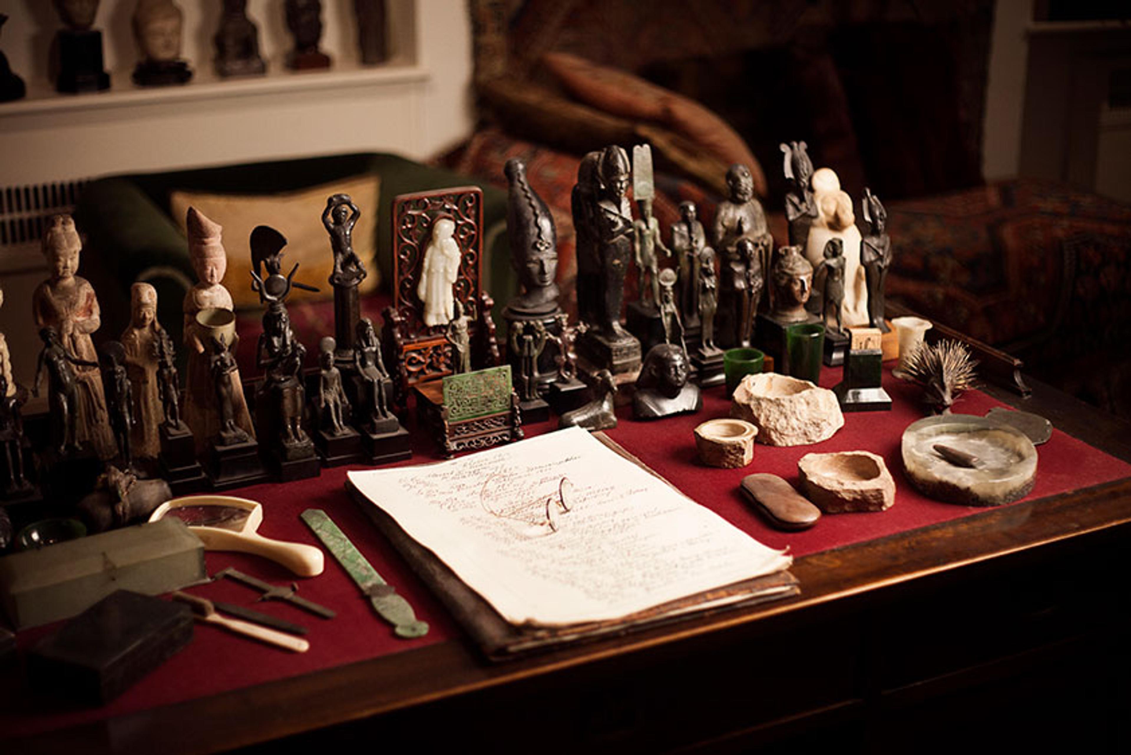 Photo of a table with various small statues, artefacts and an open notebook arranged on a red cloth.