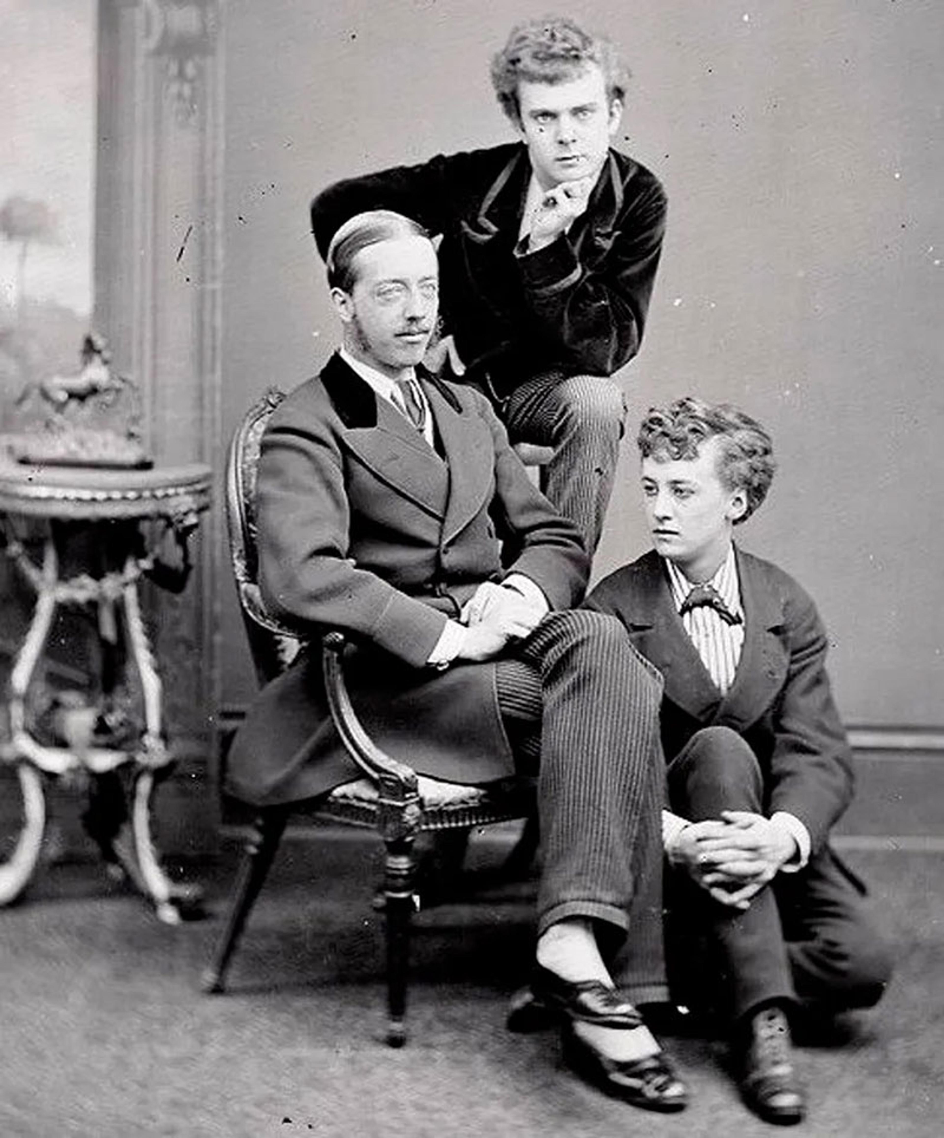 Vintage black and white photo of three people in Victorian-era suits posed in a studio setting.