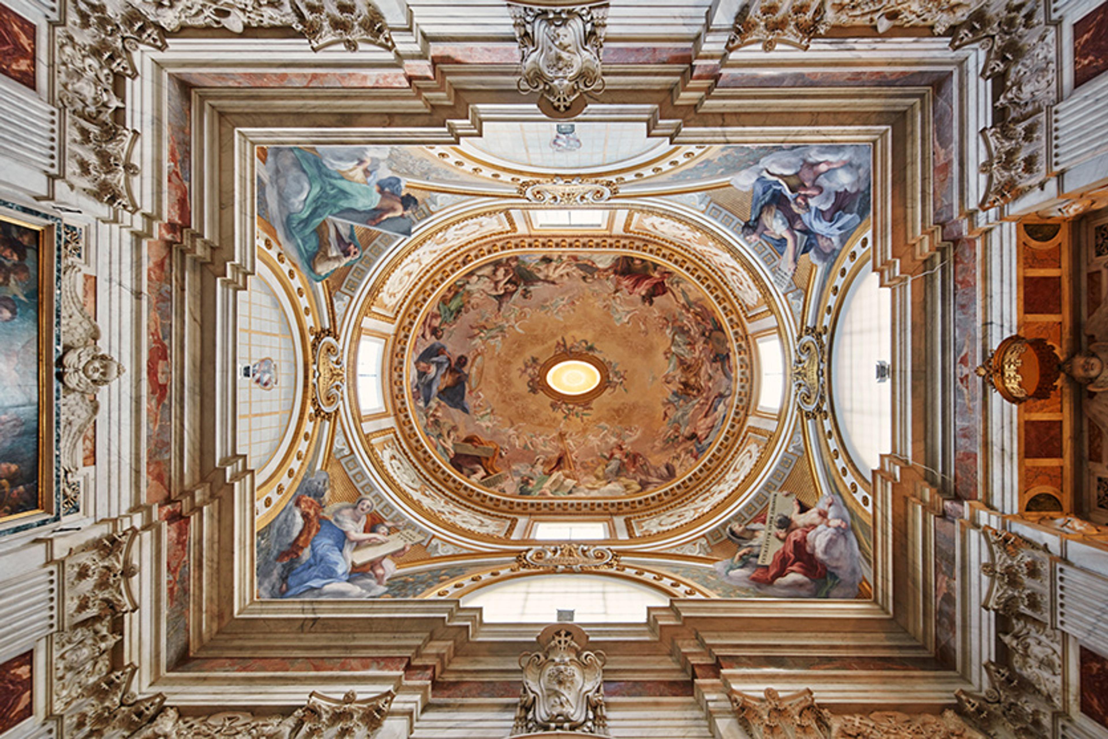 Ornately painted ceiling in a church featuring intricate frescoes of angels and cherubs in vibrant colours.