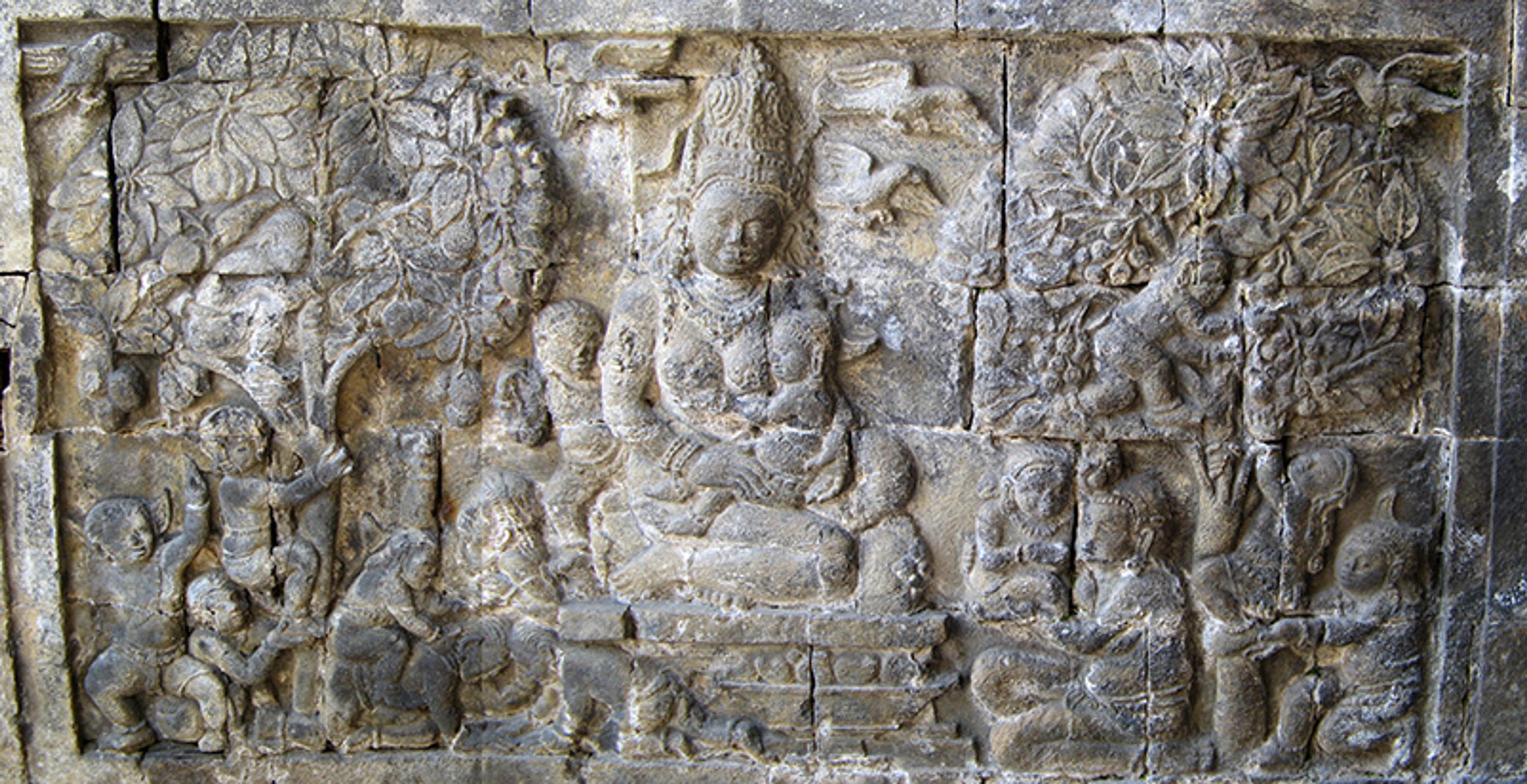 Ancient stone relief carving depicting a seated figure surrounded by trees and people, part of a historical architectural site.