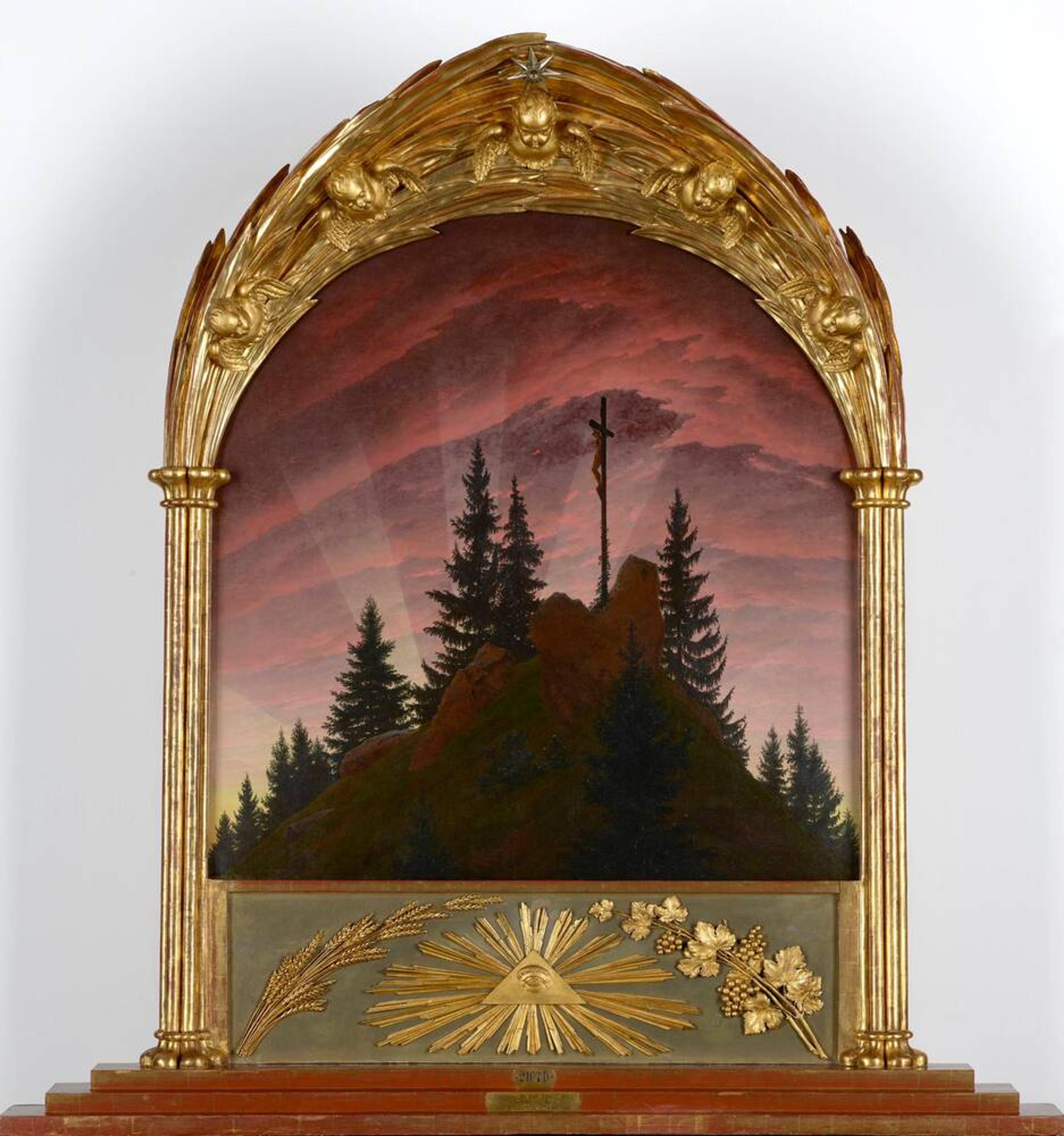 Ornate framed painting of a cross on a hill with trees at sunset adorned with gold embellishments and an eye symbol.