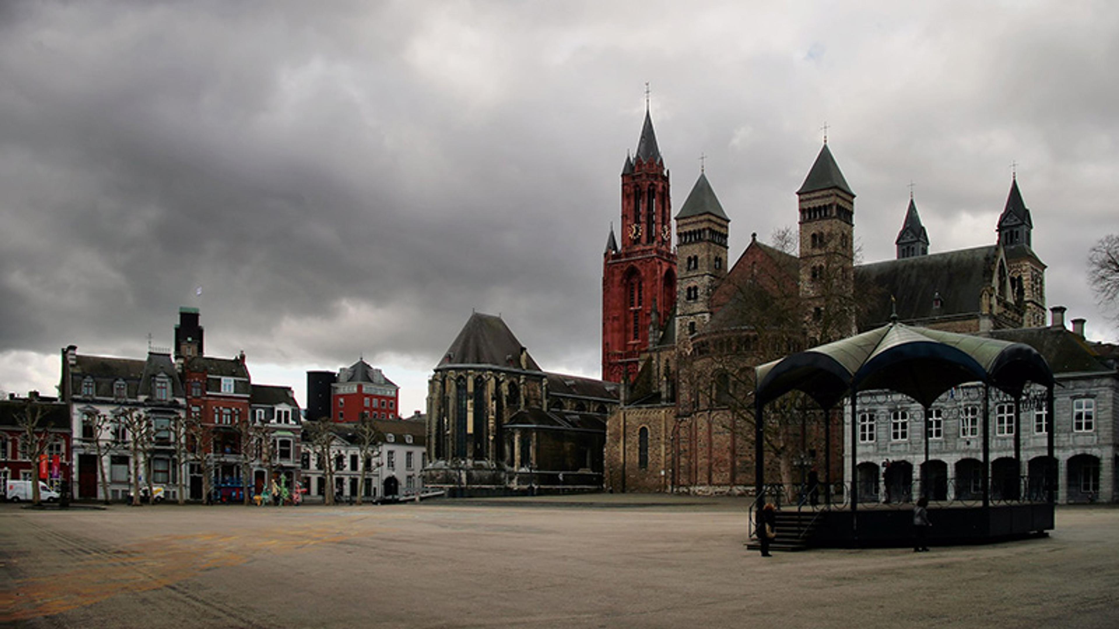 Photo of a historic European square with colourful buildings and a large church under a cloudy sky.