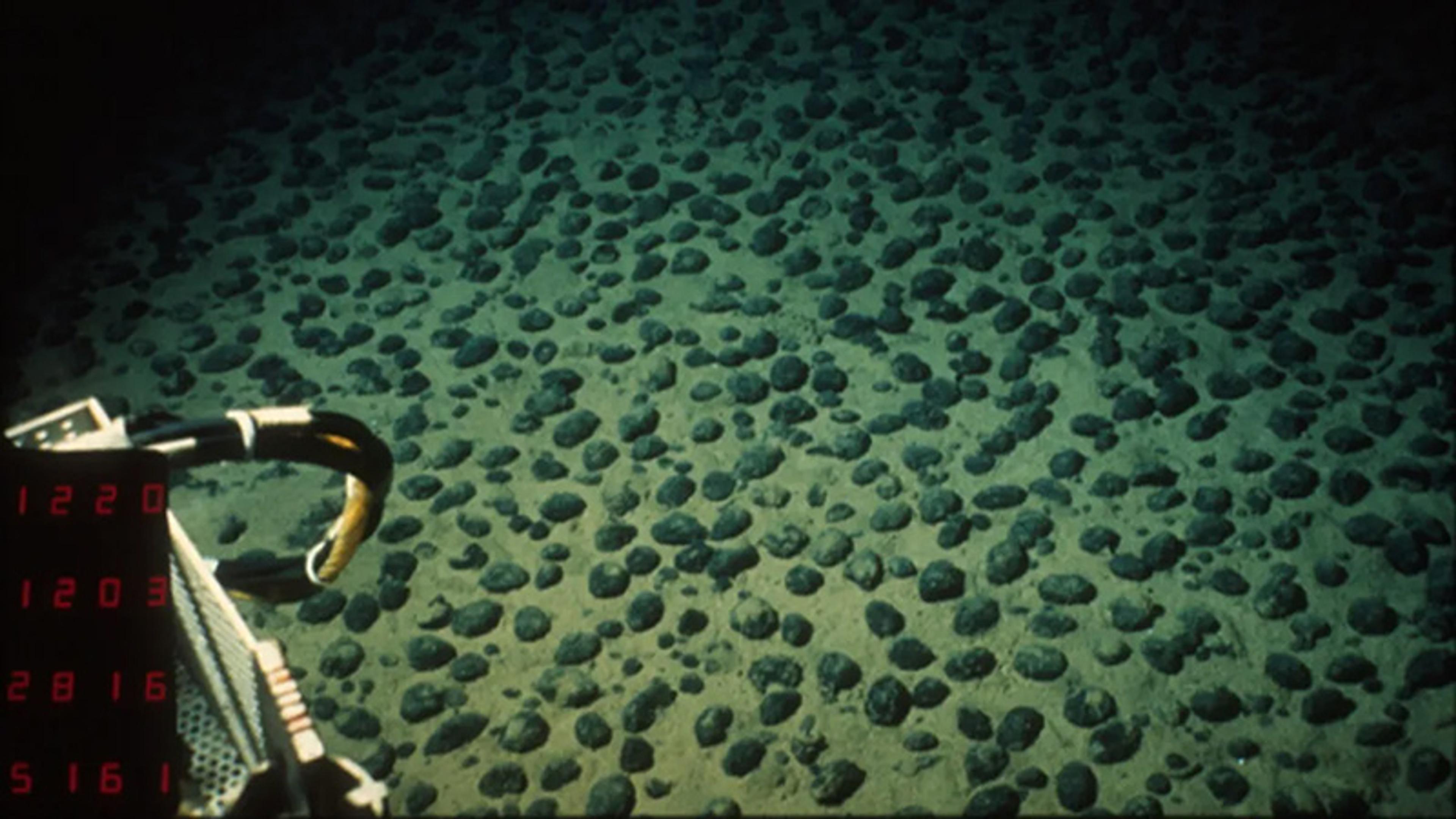 Underwater photo of a seabed with many round rocks scattered across the sand a bit of machinery visible at the edge.
