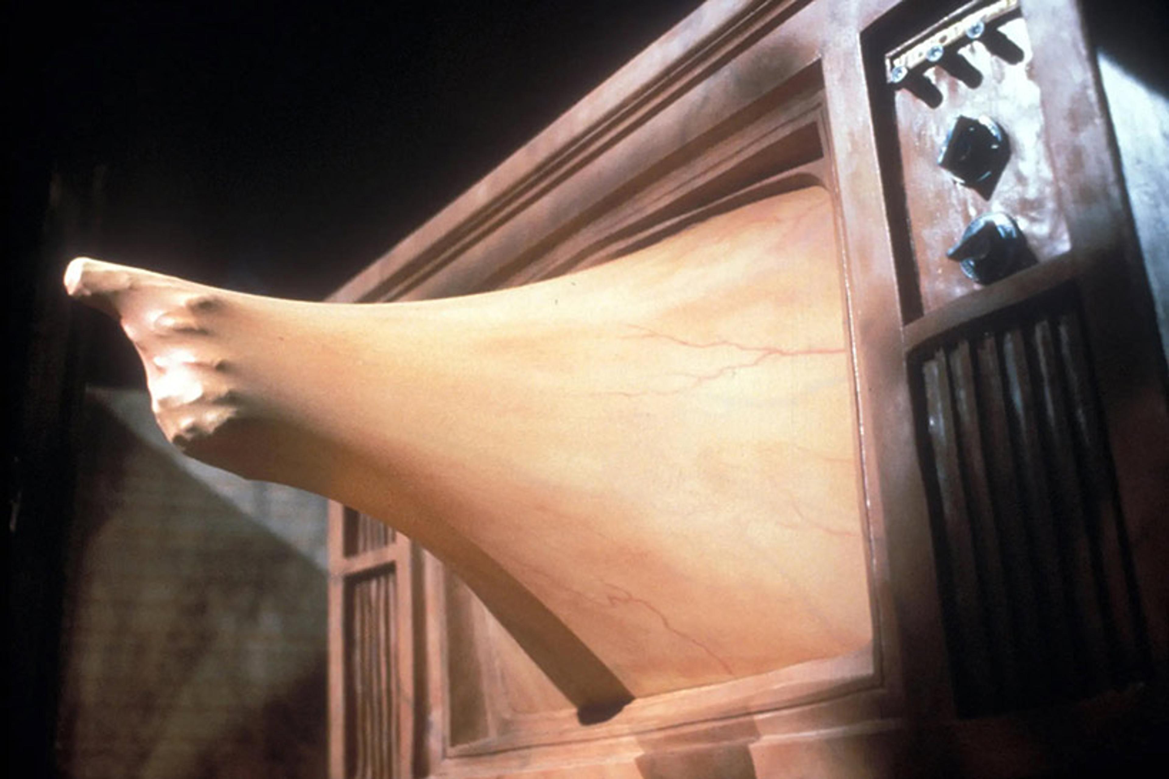 A surreal scene with a hand pushing through an old television screen, distorting the screen’s fleshy surface.