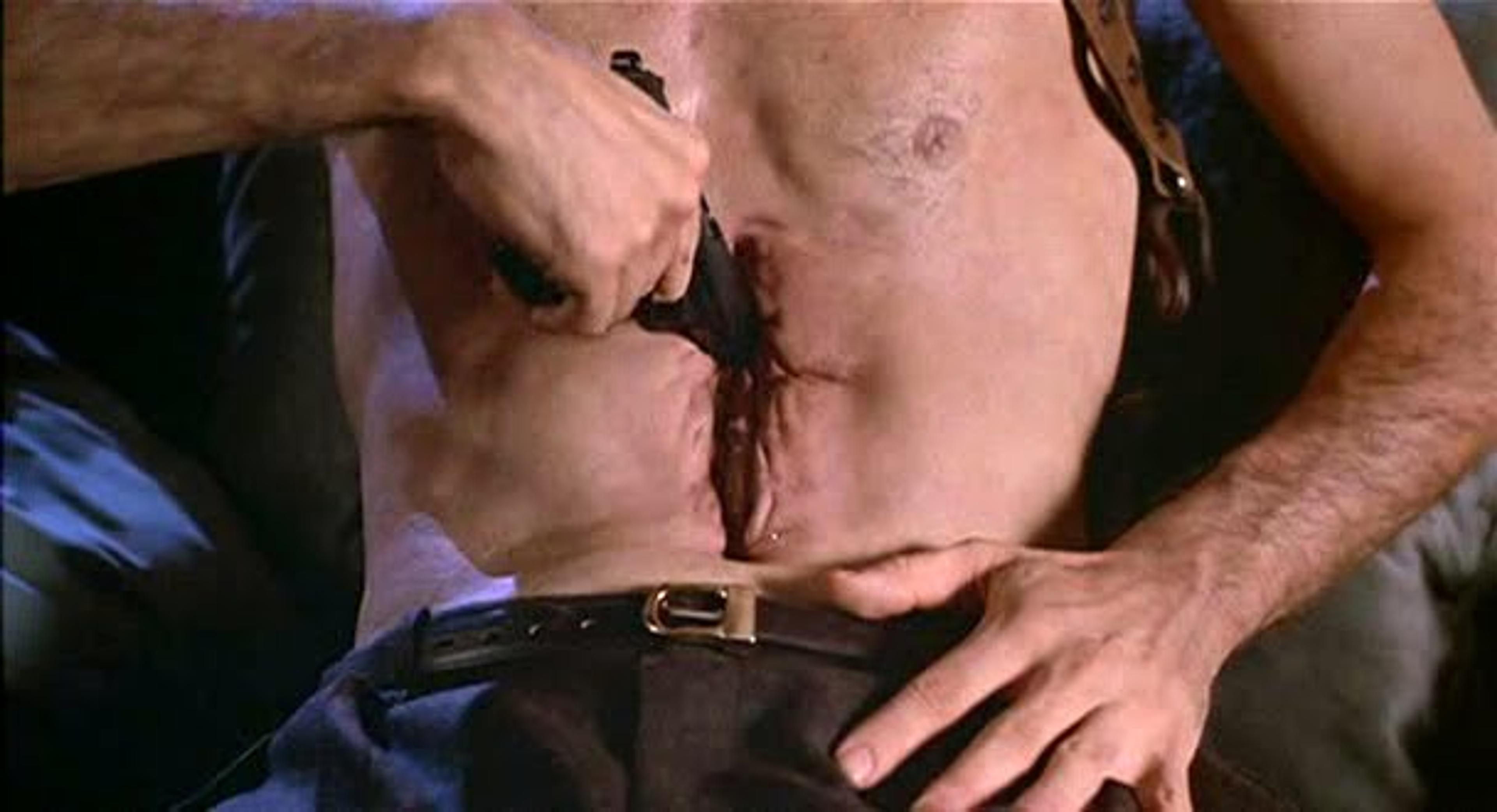 Still from a film showing a man pulling a gun from a cavity in his abdomen.