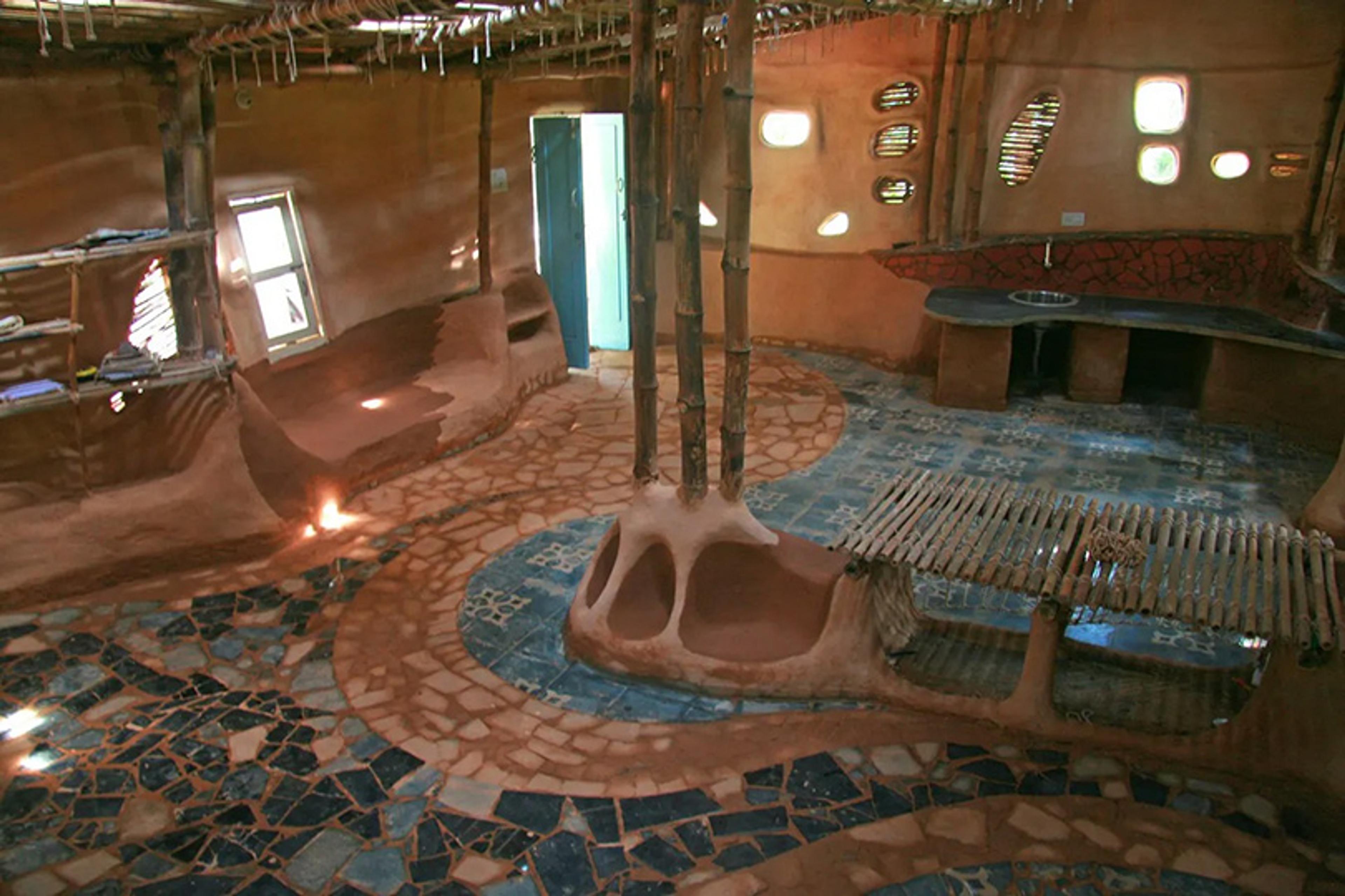 Photo of an eco-friendly room with mud walls bamboo furniture mosaic floor and unique windows inside an earthy structure.