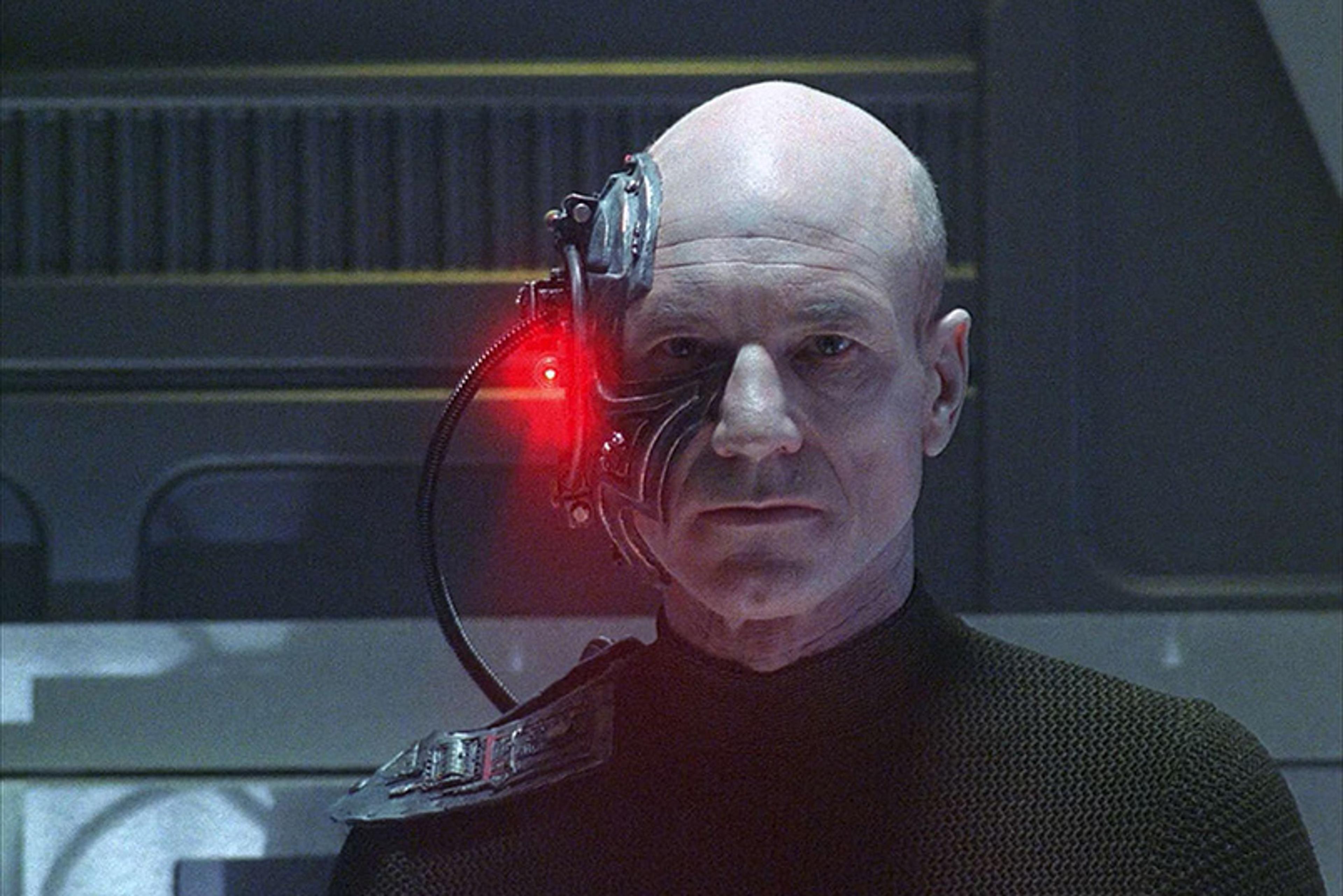 Photo of a bald man with a mechanical eye implant emitting red light, featuring futuristic background elements.
