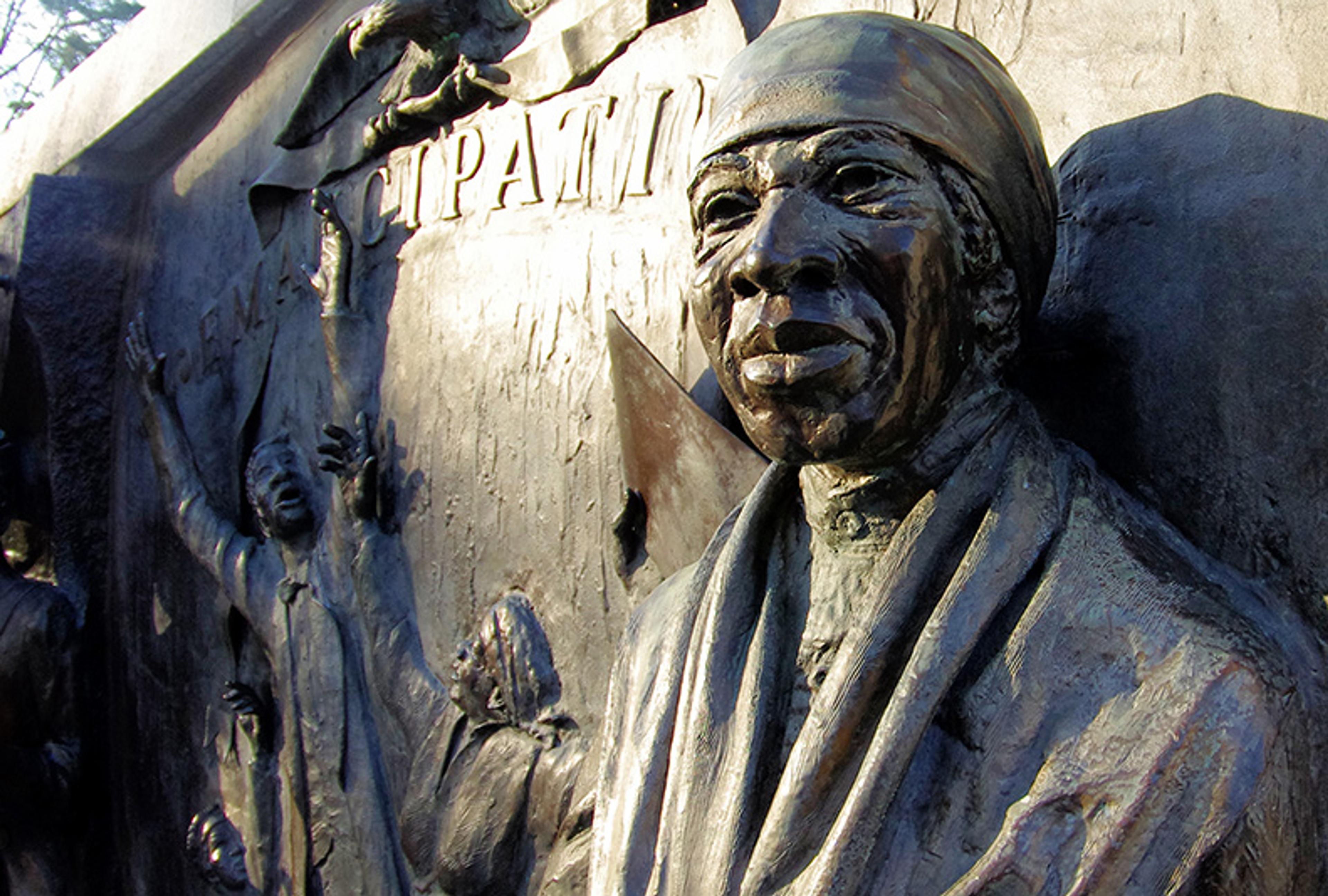 Bronze relief sculpture featuring a historical figure in a headscarf with figures and textured background, outdoor setting.