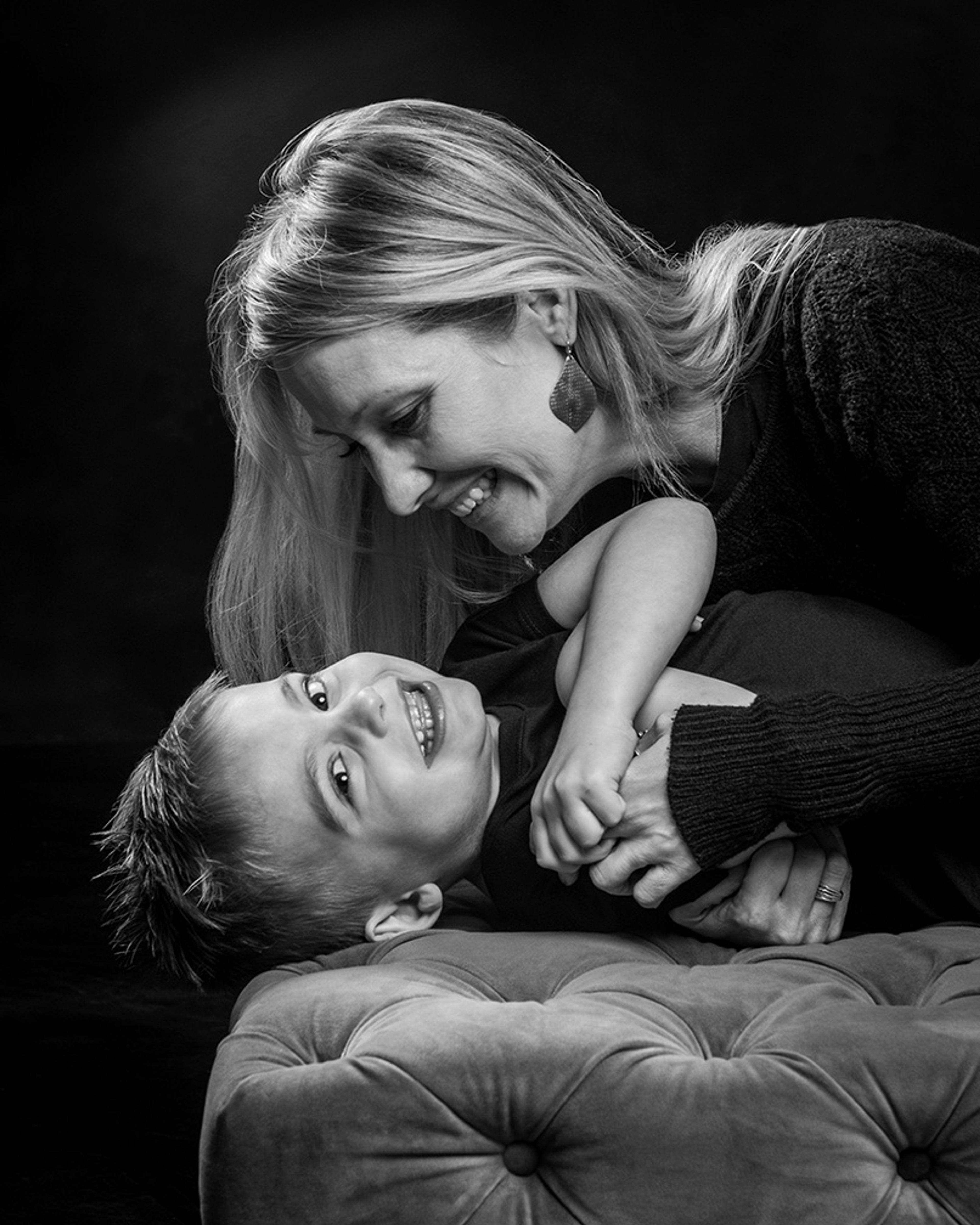 Black and white photo of a smiling woman and young boy playing on a tufted sofa.