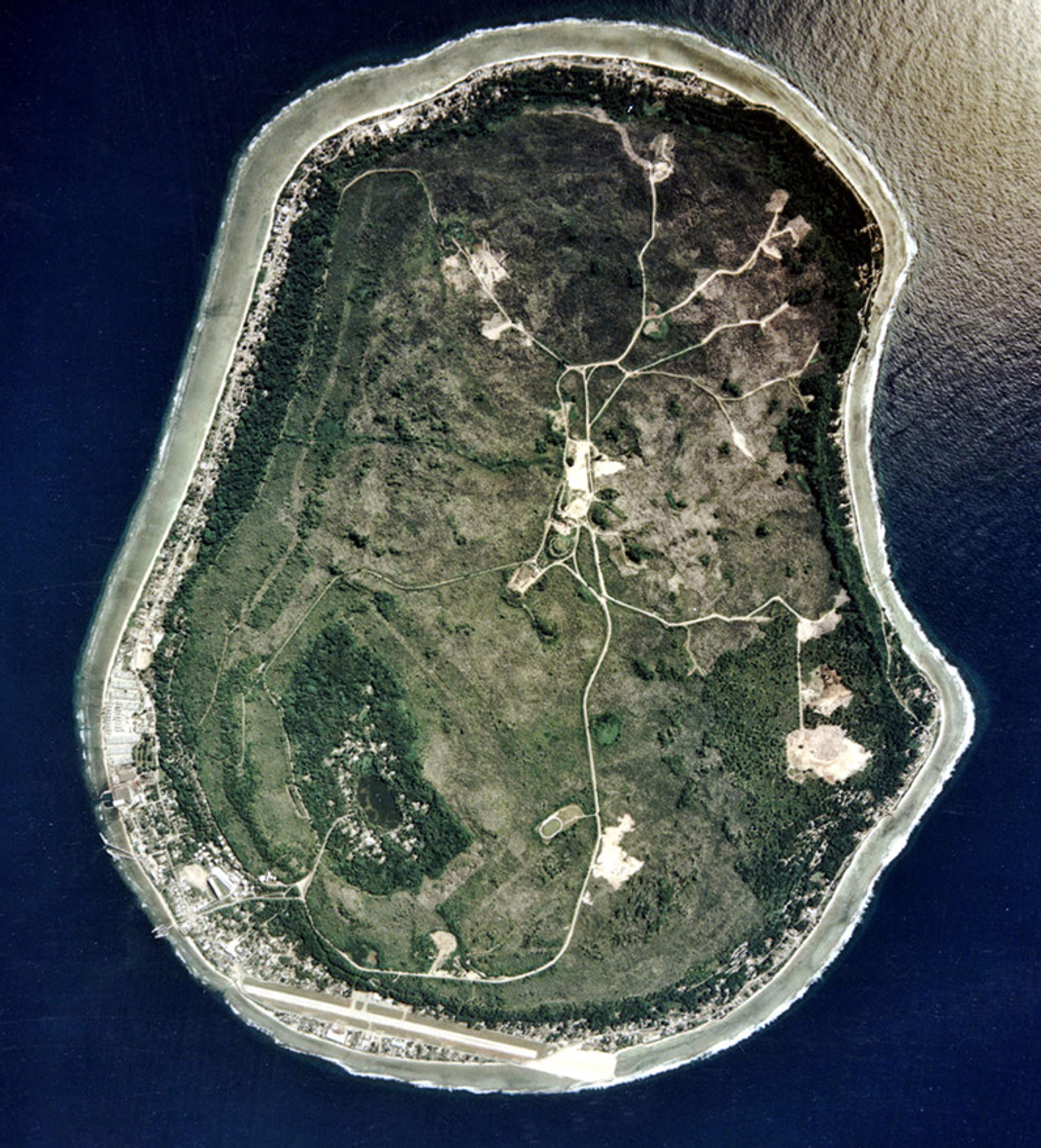 Aerial photo of a pear-shaped island surrounded by ocean, with visible roads and a small settlement along the coast.