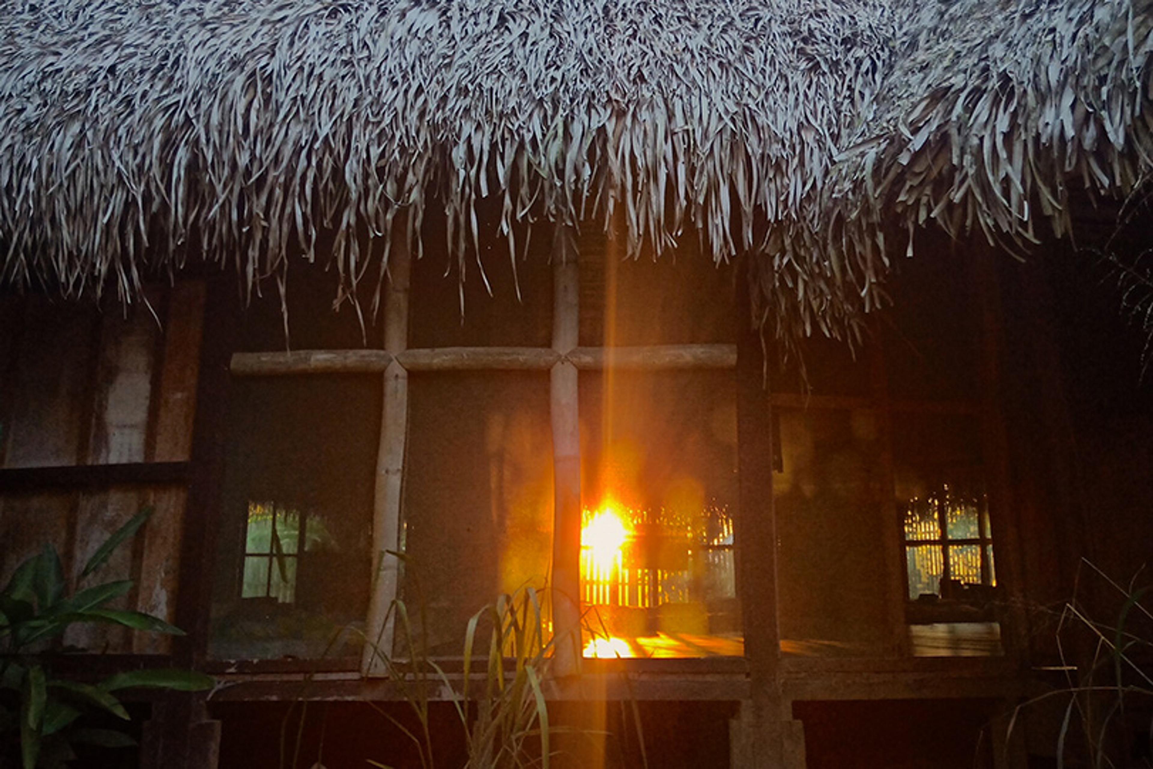 Photo of a wooden, thatched-roof hut with sunset light coming through the window
