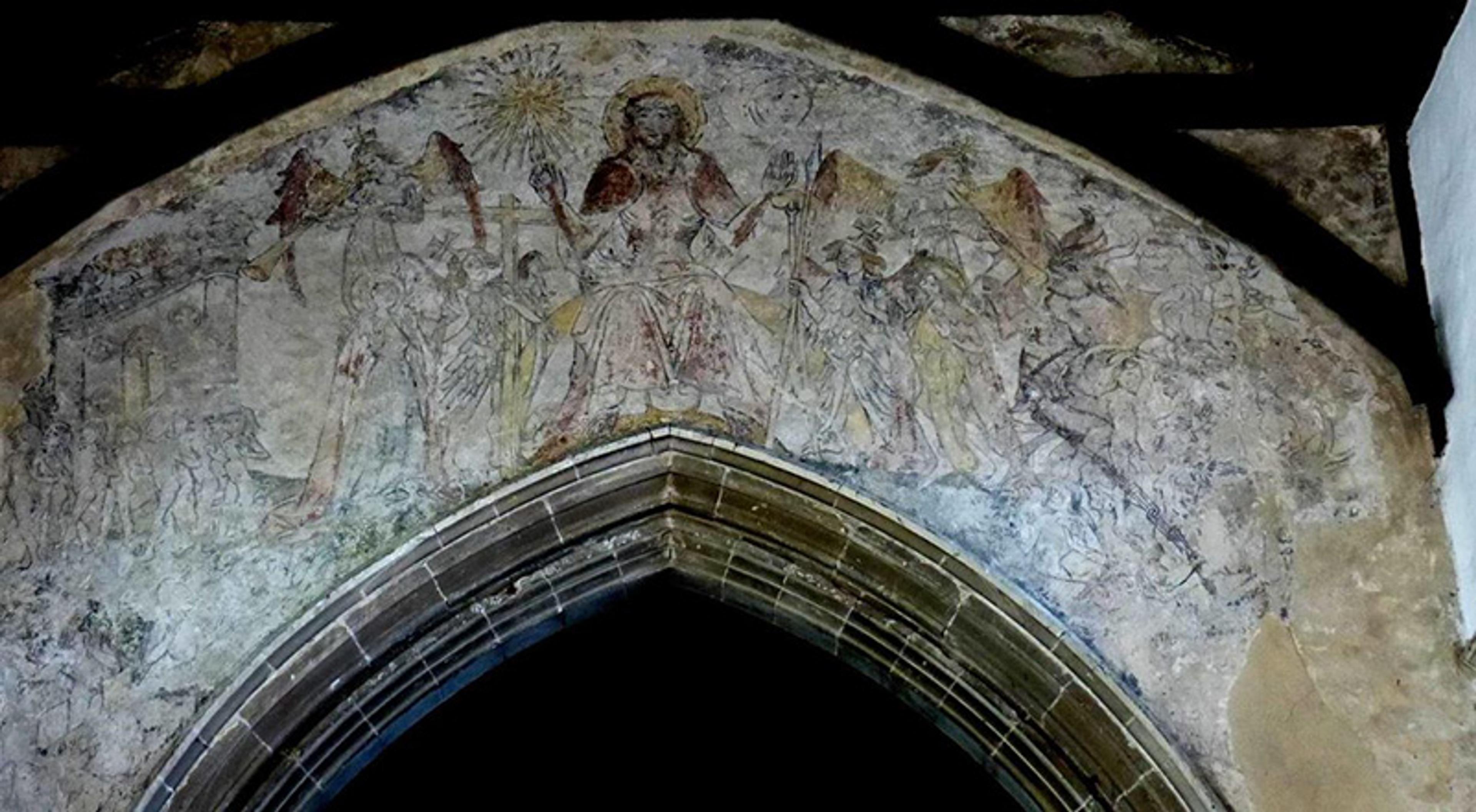 Medieval fresco above an archway depicting religious figures and scenes, featuring a central haloed figure, in a church setting.