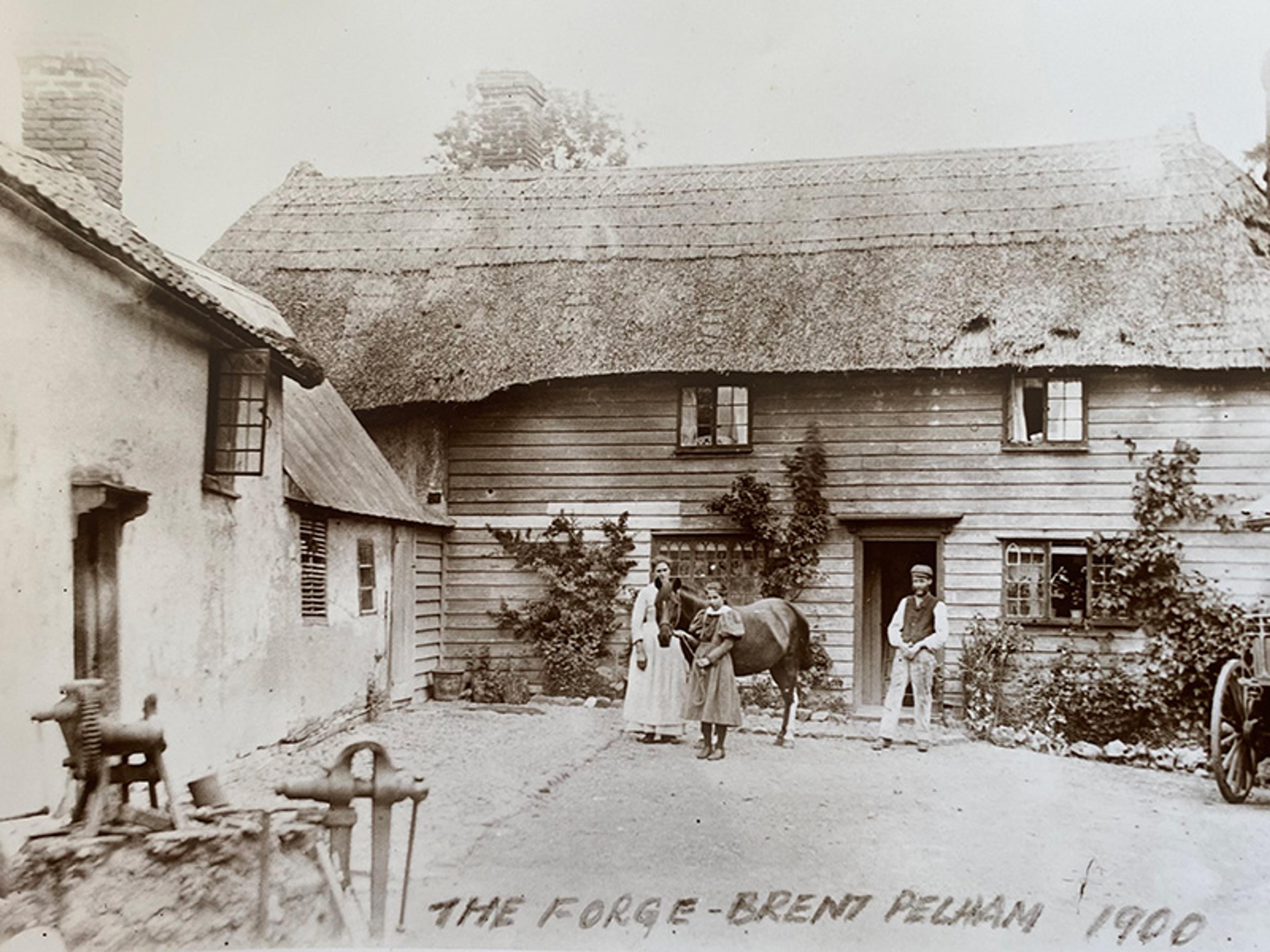 Vintage photo of a thatched forge in Brent Pelham, 1900 with people and a horse in front, showcasing rural life.
