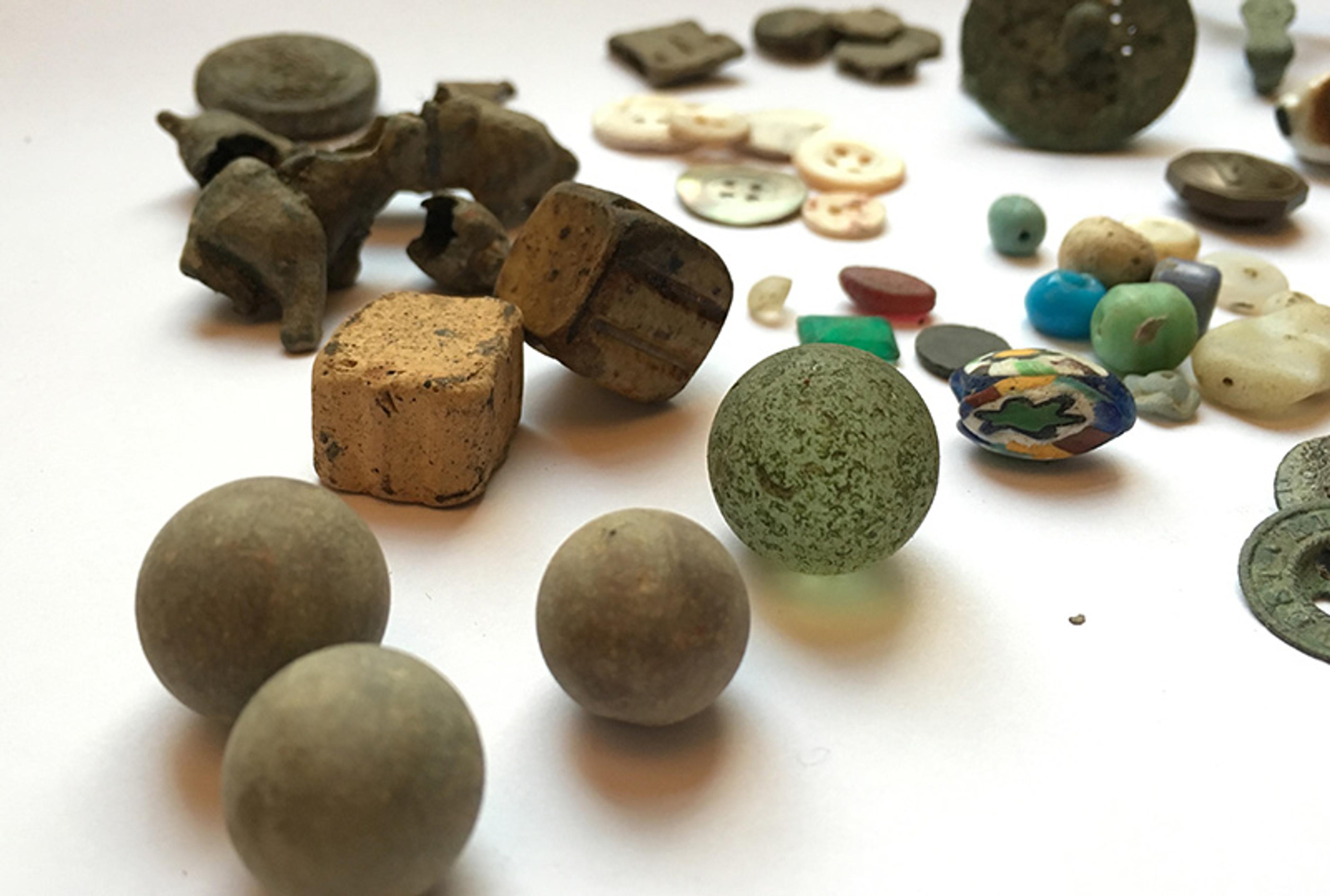 Assorted small artefacts on a white surface, including buttons, marbles and fragments in various shapes and colours.