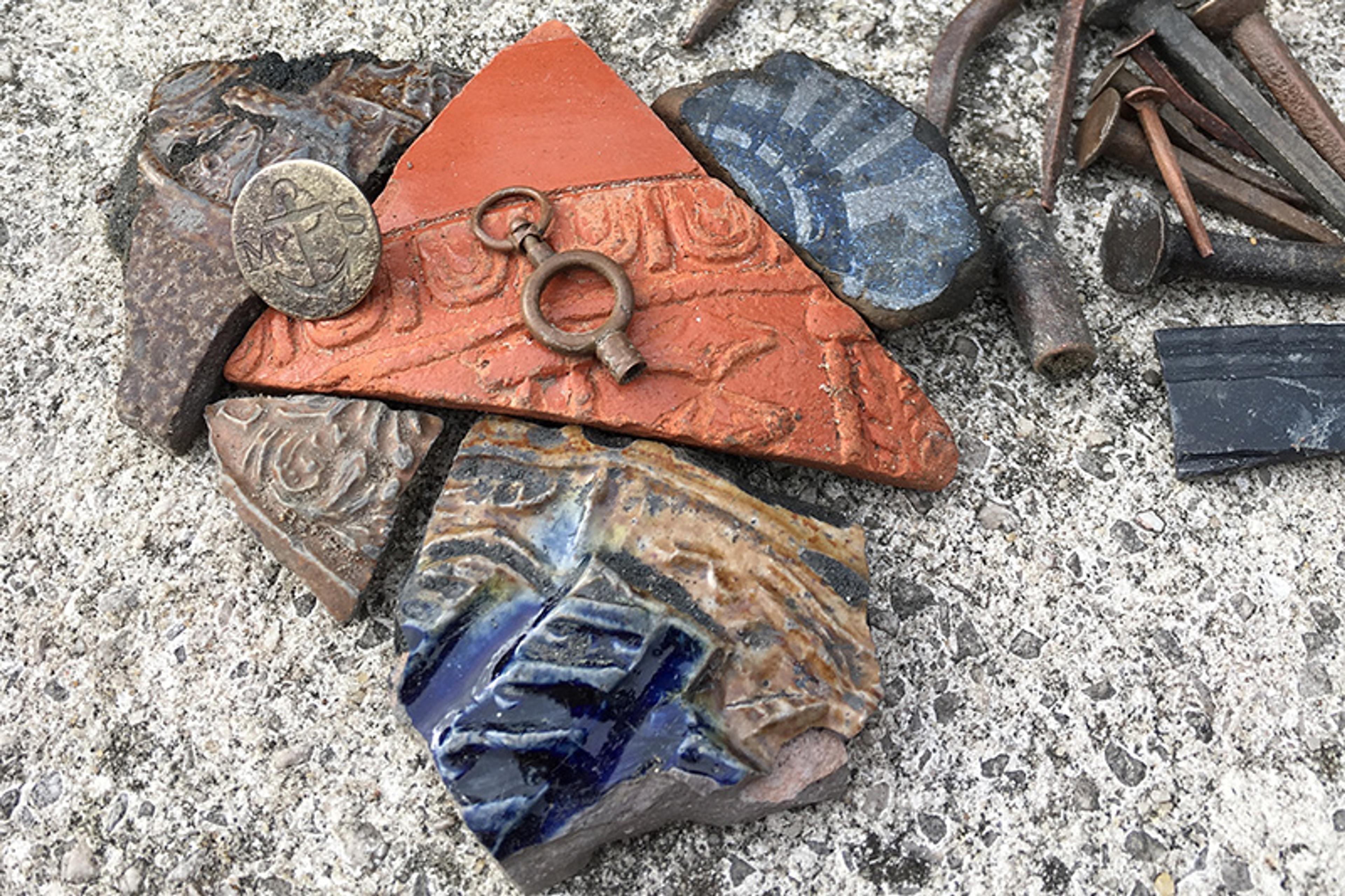 Assorted pottery shards and a button placed on a textured surface among metal nails and tools.