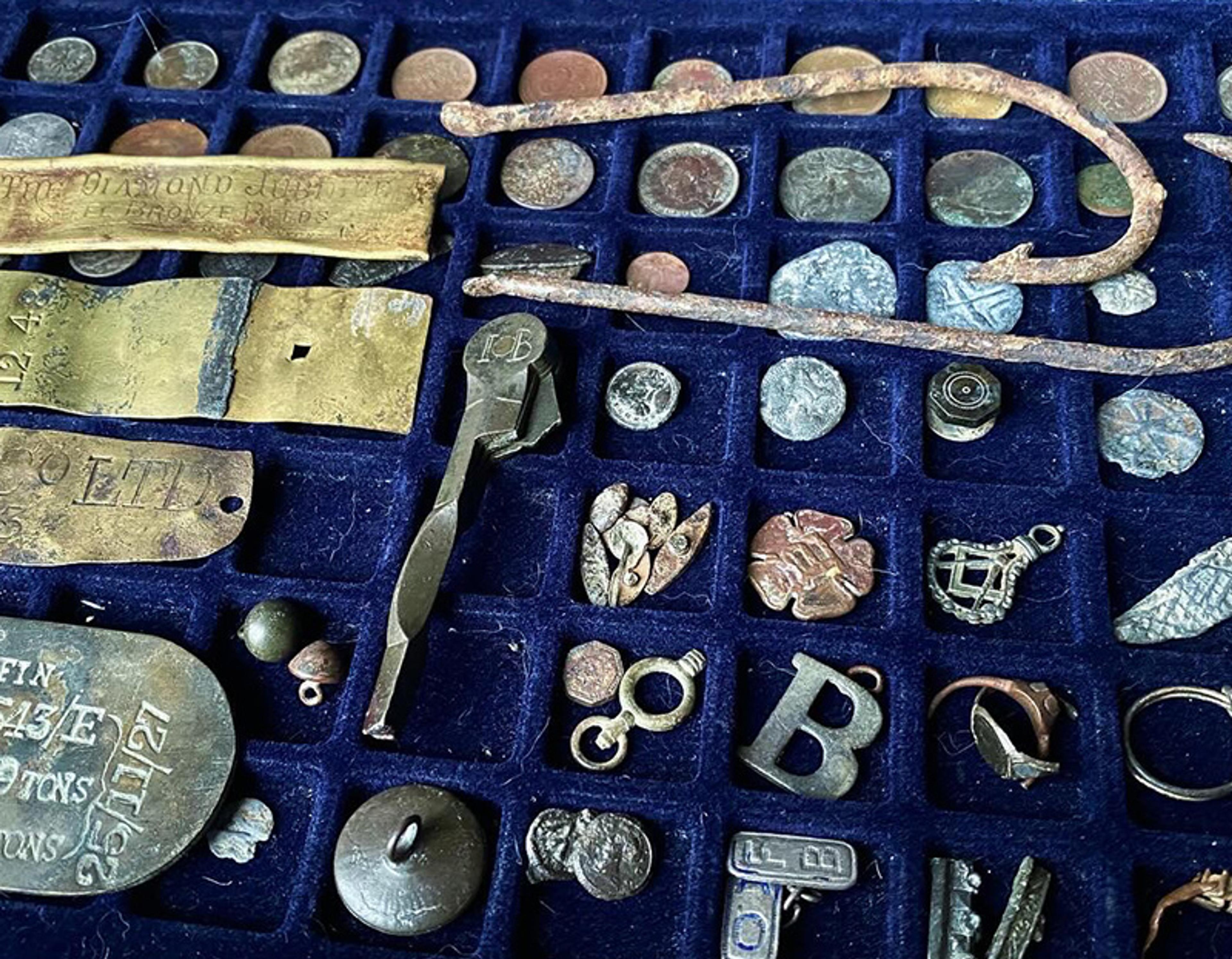 Assorted metal relics displayed on a navy blue grid, including coins and decorative items.