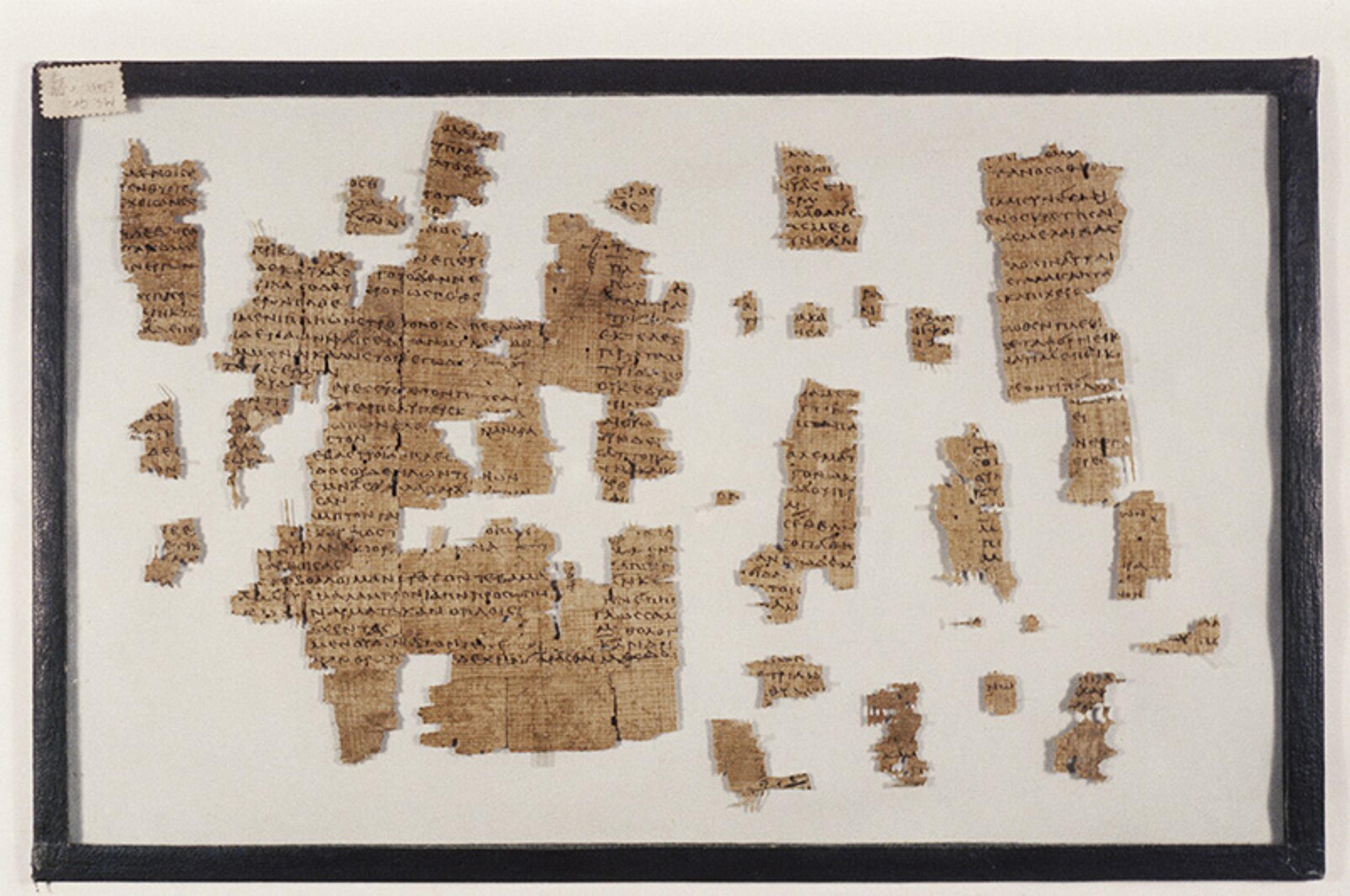 Photograph of ancient papyrus fragments with Greek text displayed in a black frame on a white background.