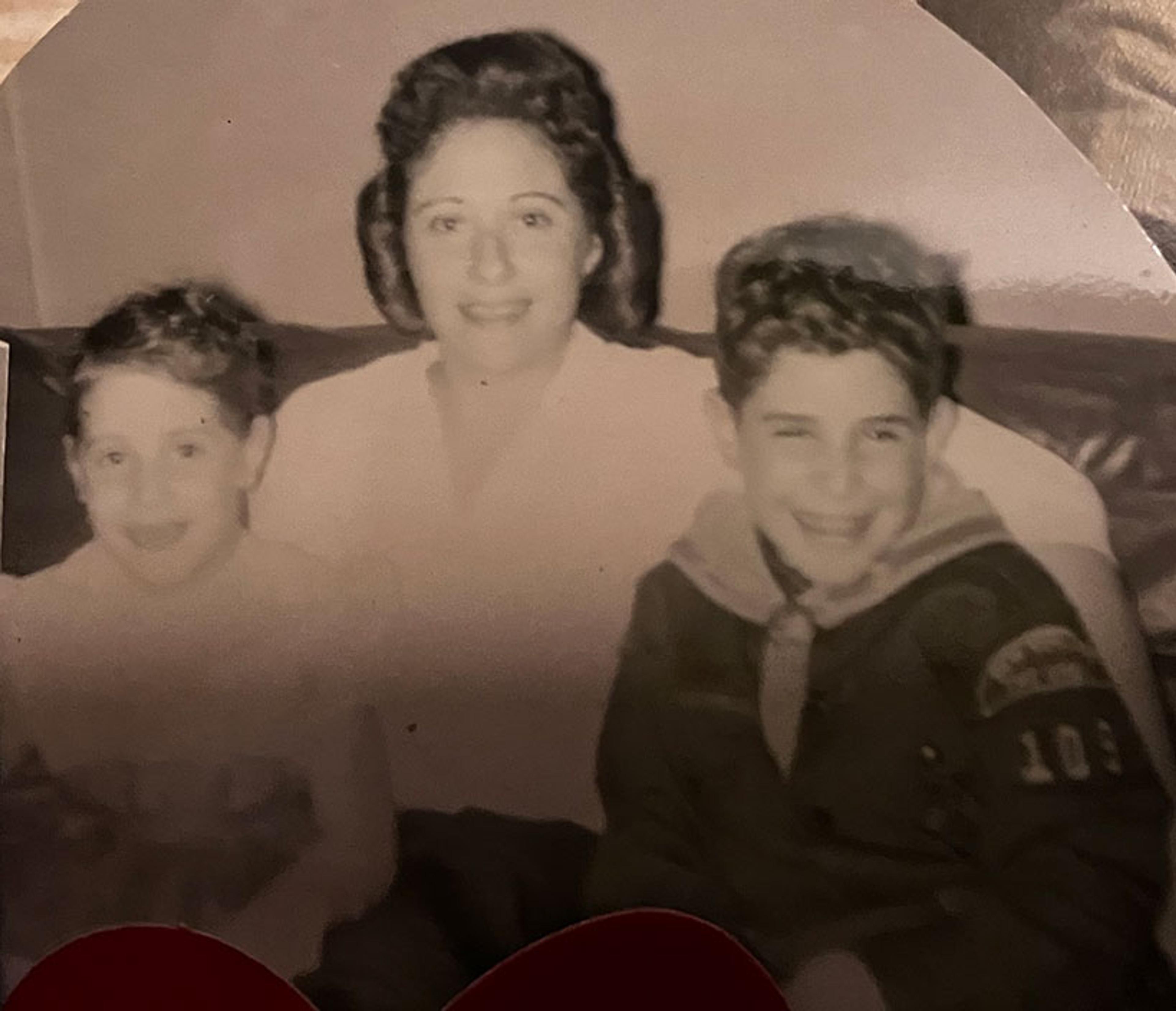 Vintage black and white photo of a woman sitting with two young children on a sofa, all smiling warmly at the camera.