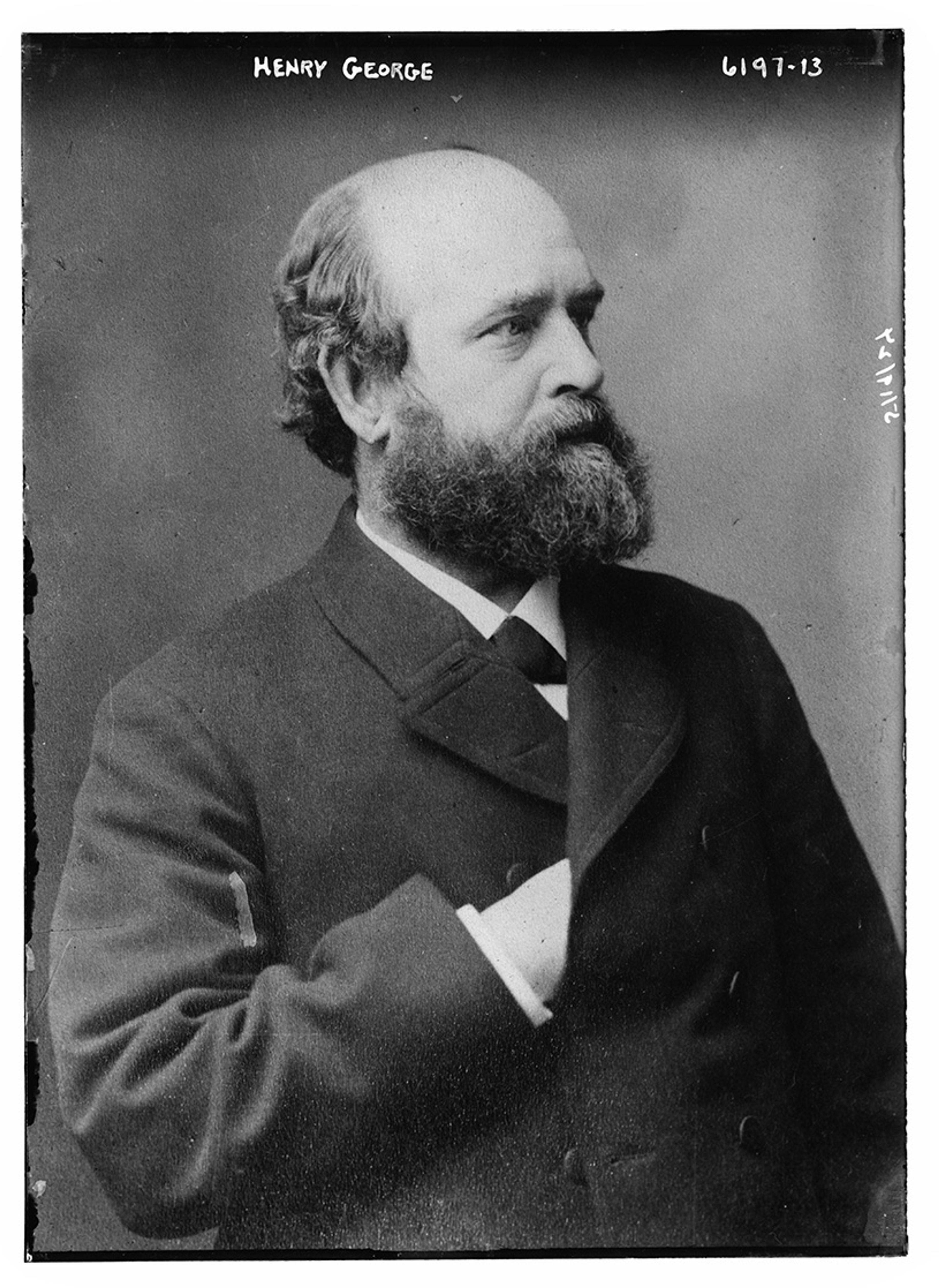Black and white photo of a bearded man in a suit with his hand inside his coat photographed in profile.