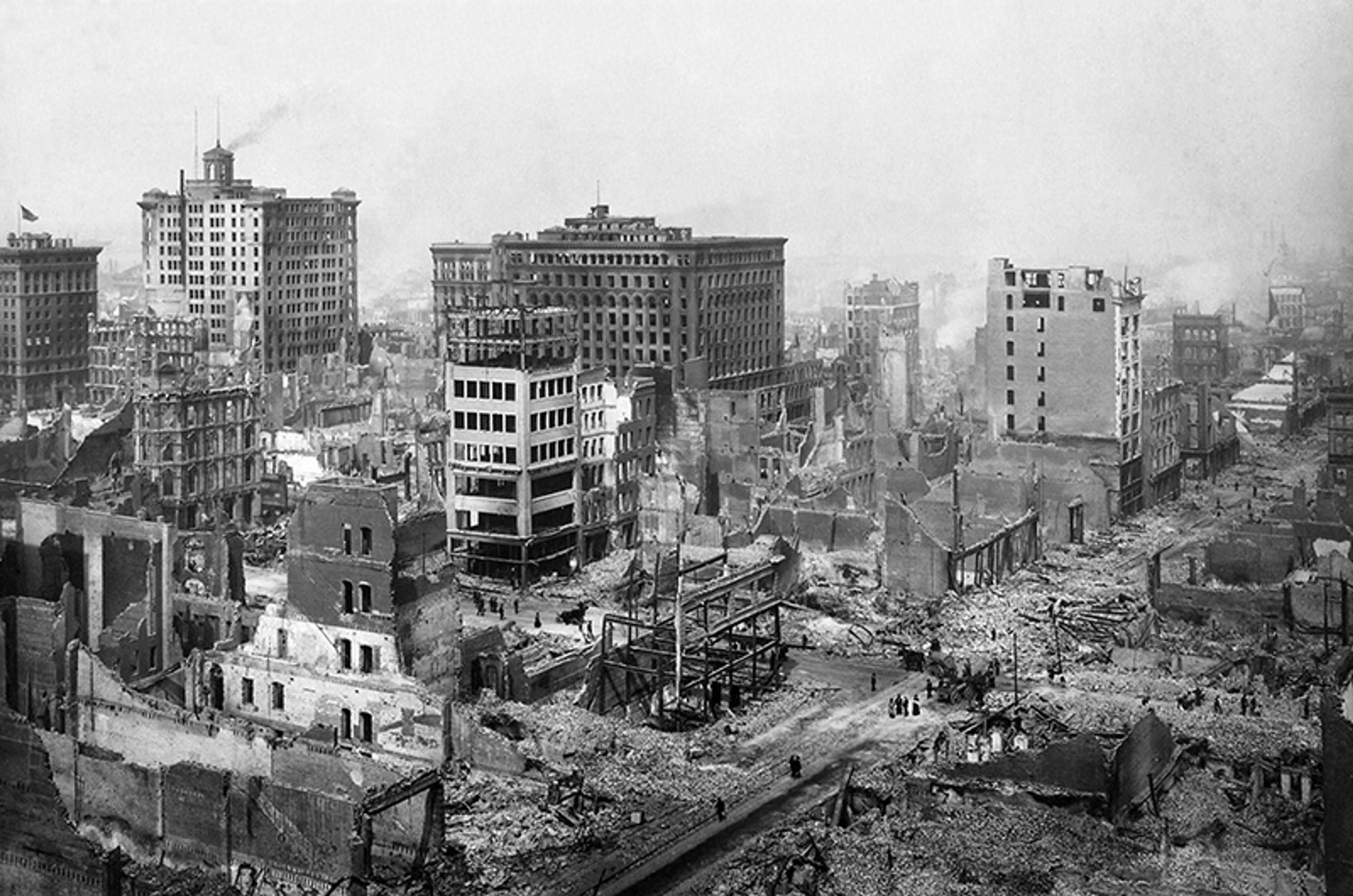Black and white photo of a cityscape with buildings in ruins, debris scattered, and several tall structures still standing.