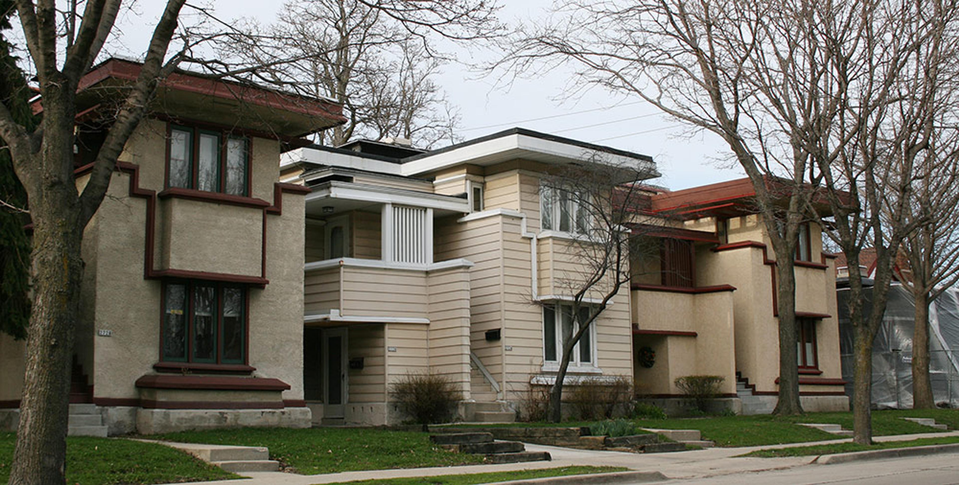 A row of early 20th-century houses with geometric designs and flat roofs, framed by leafless trees.
