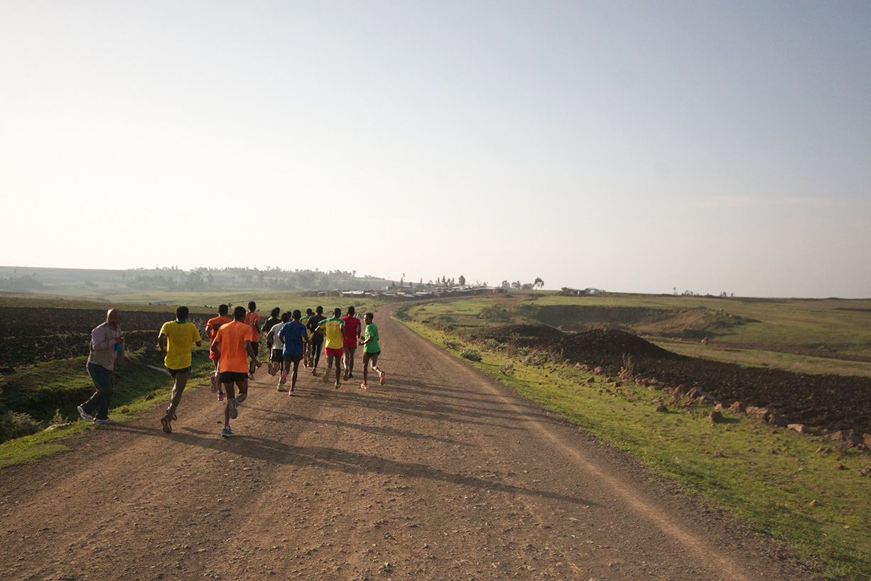 Un grupo de corredores con atuendos coloridos en un camino de tierra en un paisaje rural bajo un cielo despejado.
