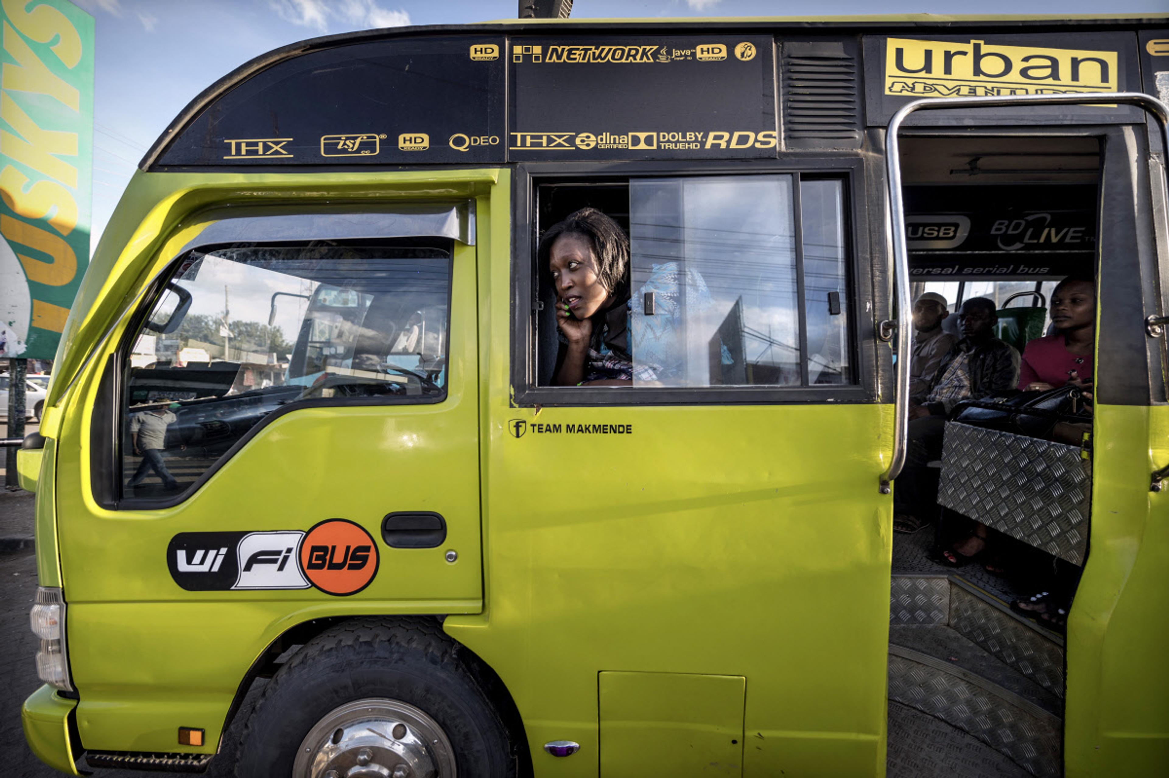 A bright green bus with passengers seated inside, one woman looks out of the window, Wi-Fi logo on the side.