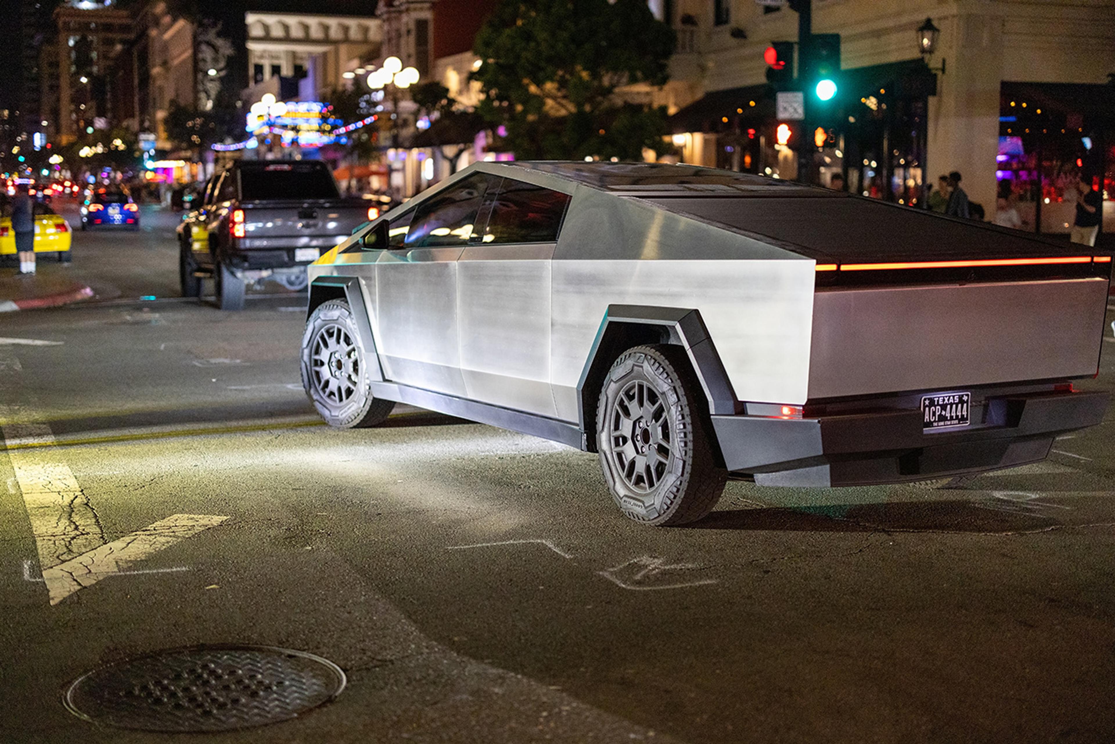 Futuristic vehicle on a city street at night, surrounded by other cars and colorful lights.