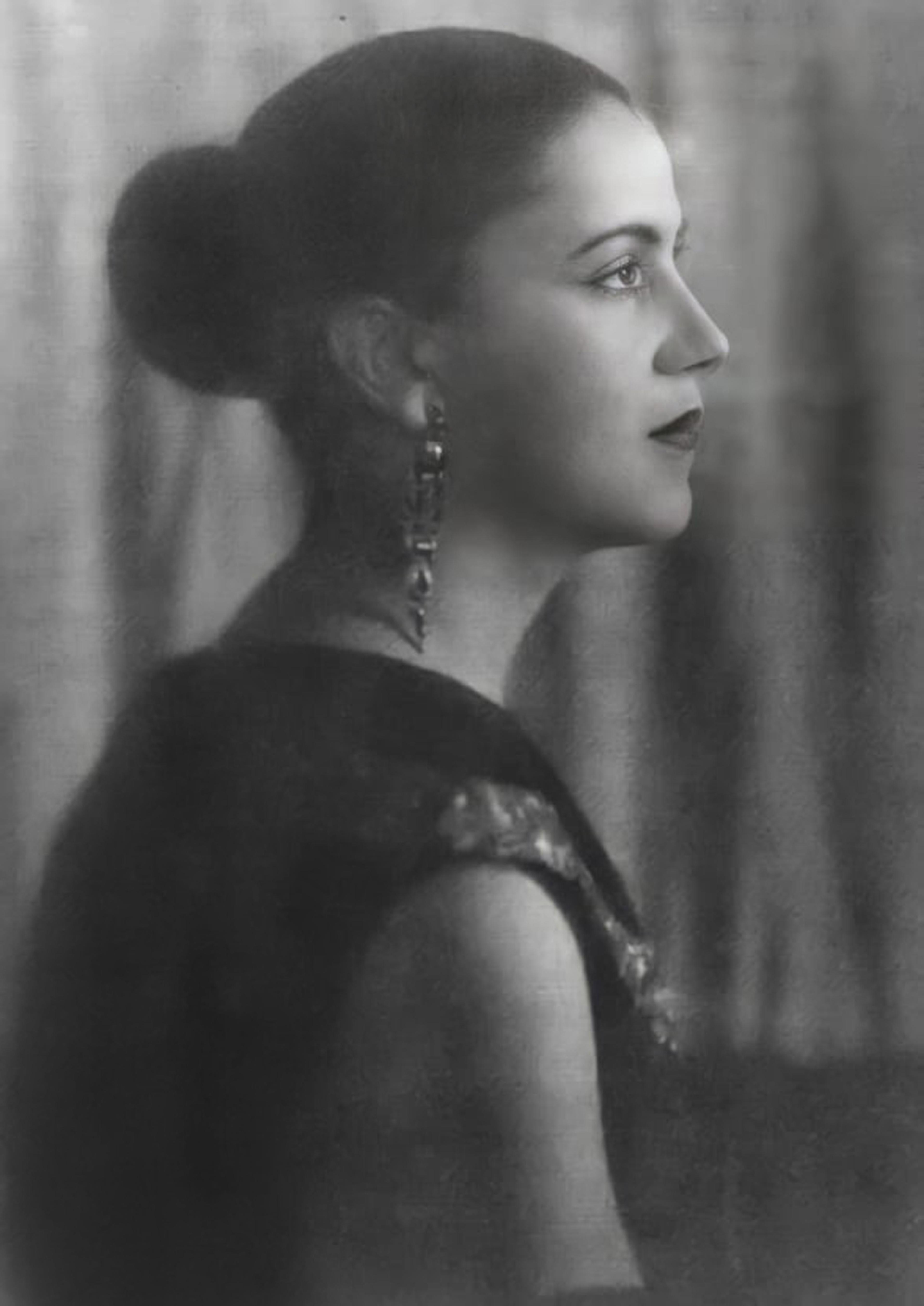 Black and white photo of a woman in profile with hair in a bun wearing earrings and a dark top, set against a blurred backdrop.