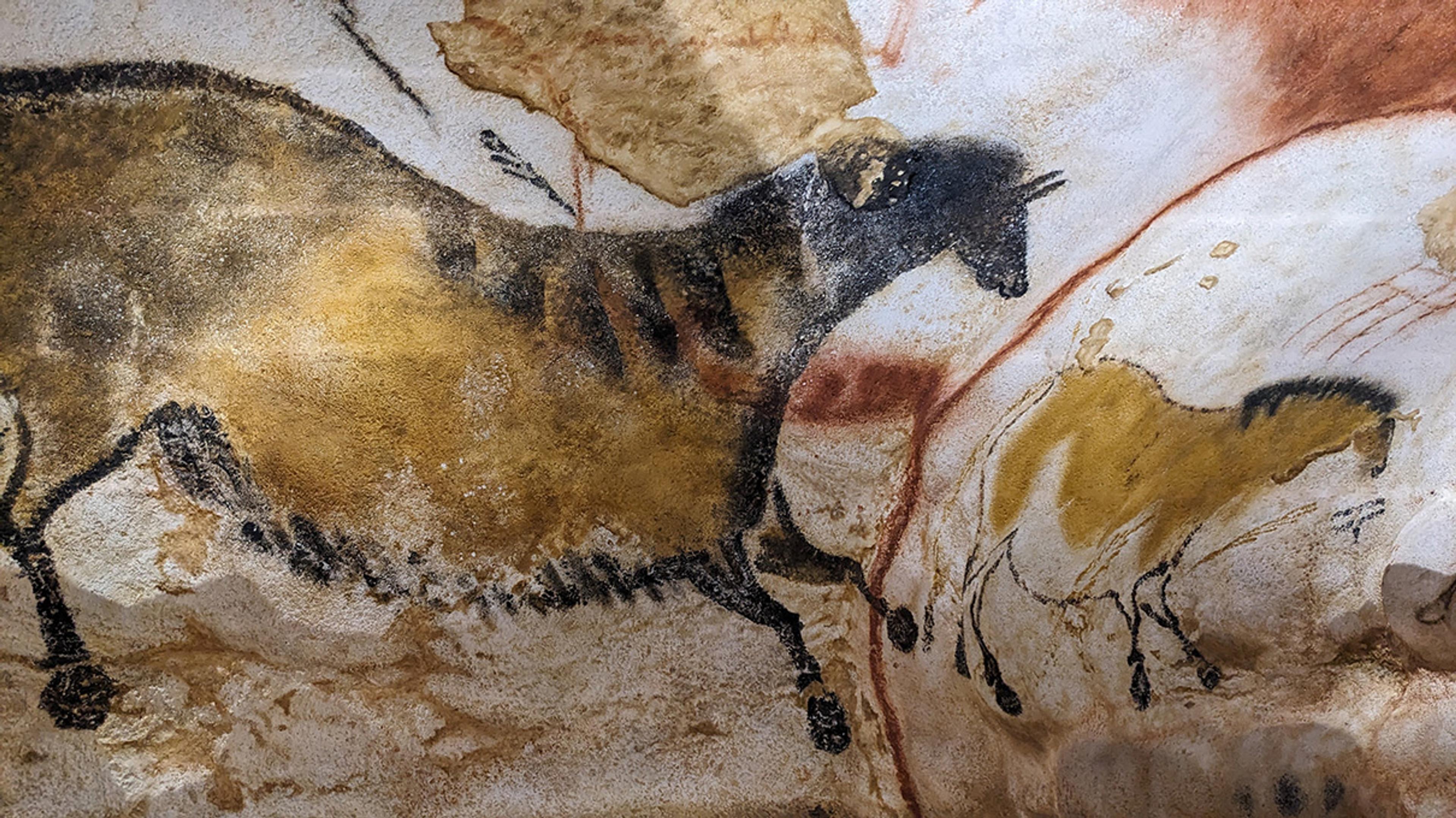 Cave painting of prehistoric animals in earthy tones on a textured rock surface.