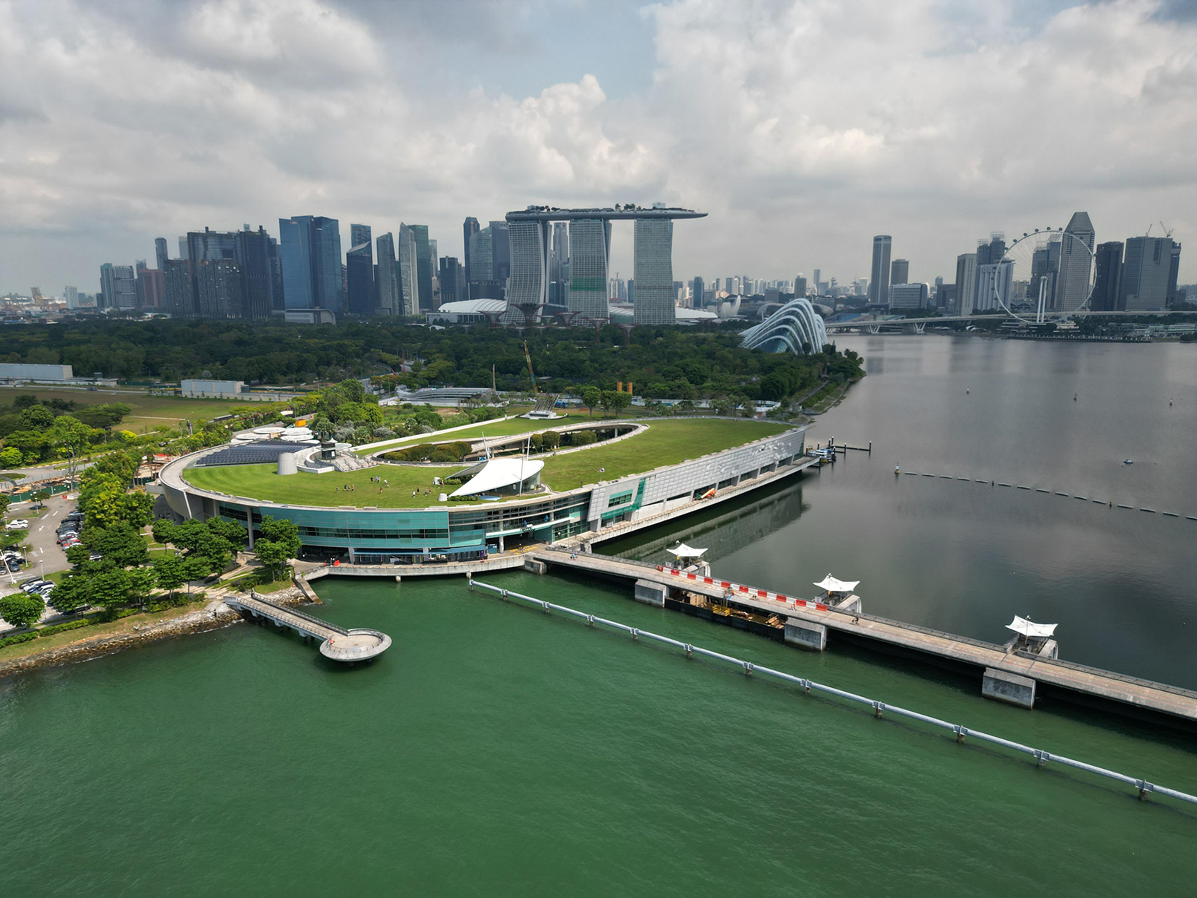 Aerial photo of Marina Barrage in Singapore with a city skyline, green roof, water views and cloudy sky.