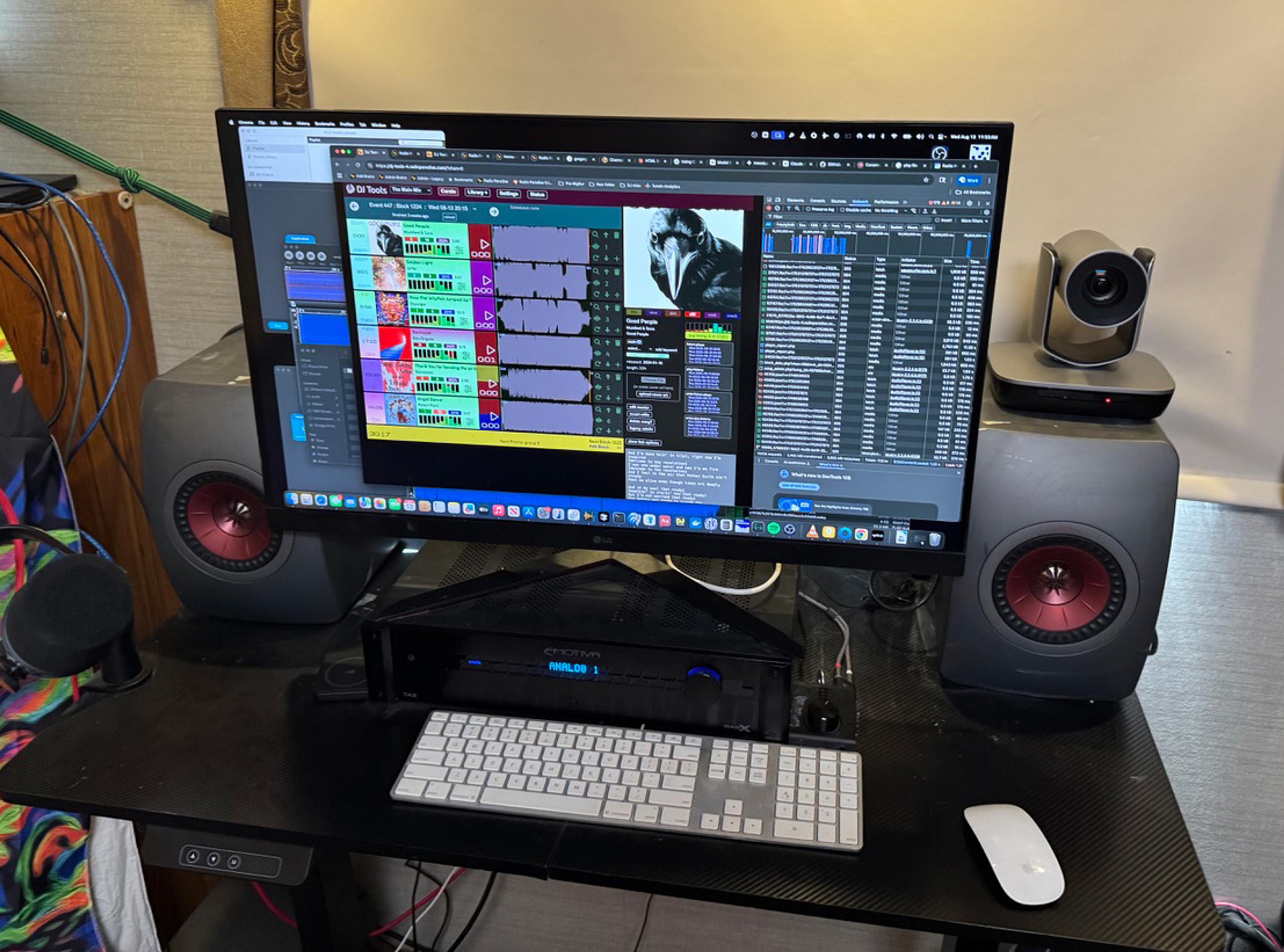 A workstation with a large monitor displaying audio editing software, flanked by speakers and a webcam.