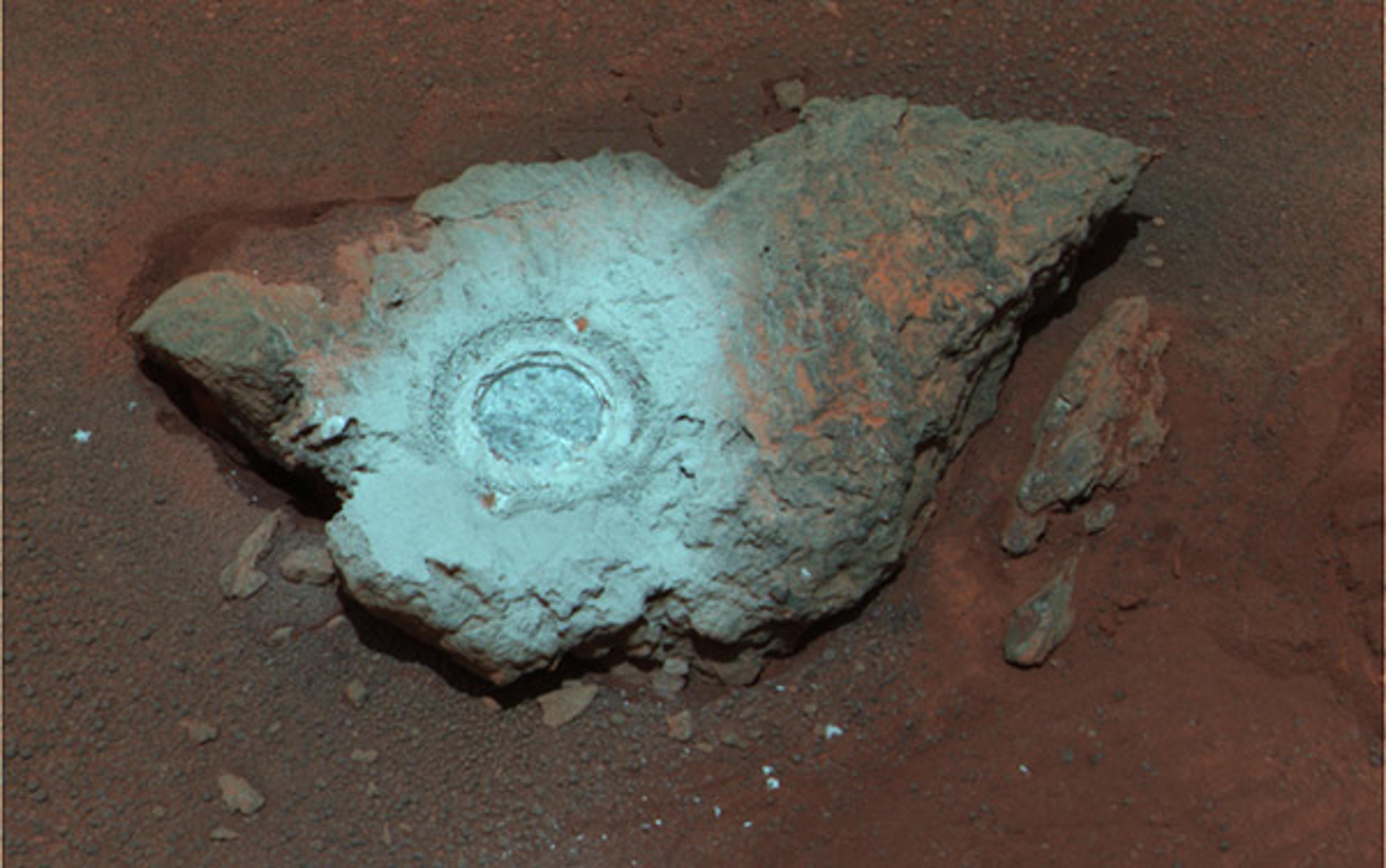 A rock on a reddish surface with a circular depression in the centre, showing a mix of grey and reddish hues.