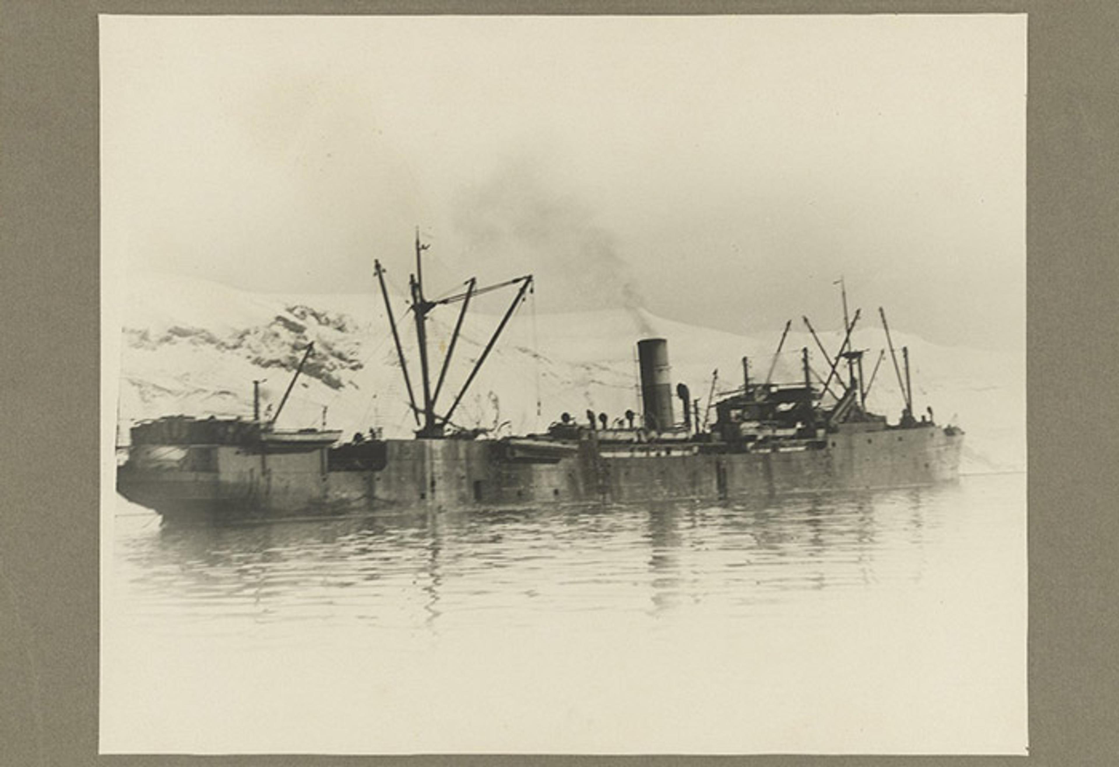 Vintage photo of an old steamship with cranes in icy waters, surrounded by snow-covered mountains in the background.