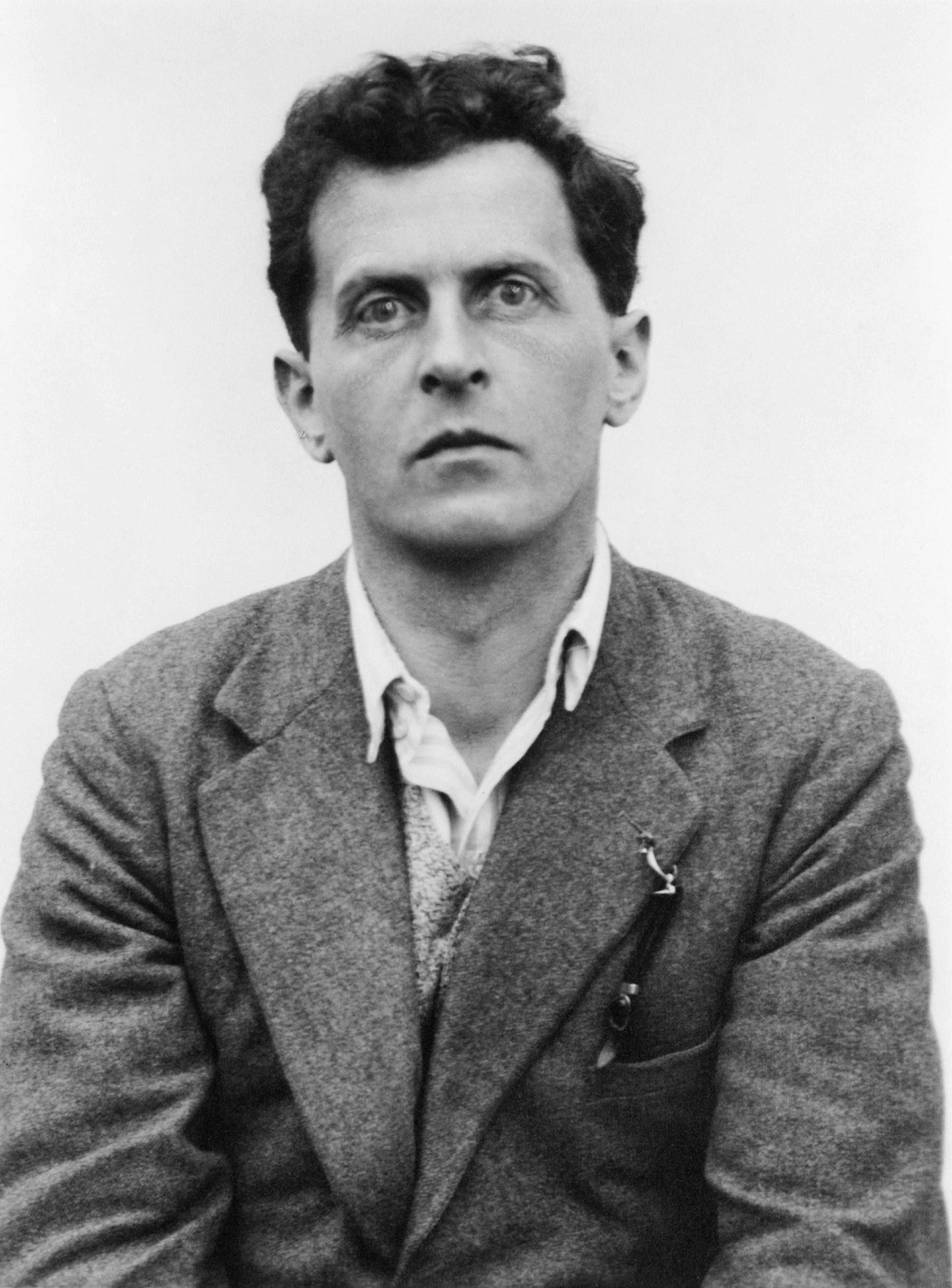 Black and white photo of a man in a suit and open-collared shirt looking directly at the camera against a plain background.