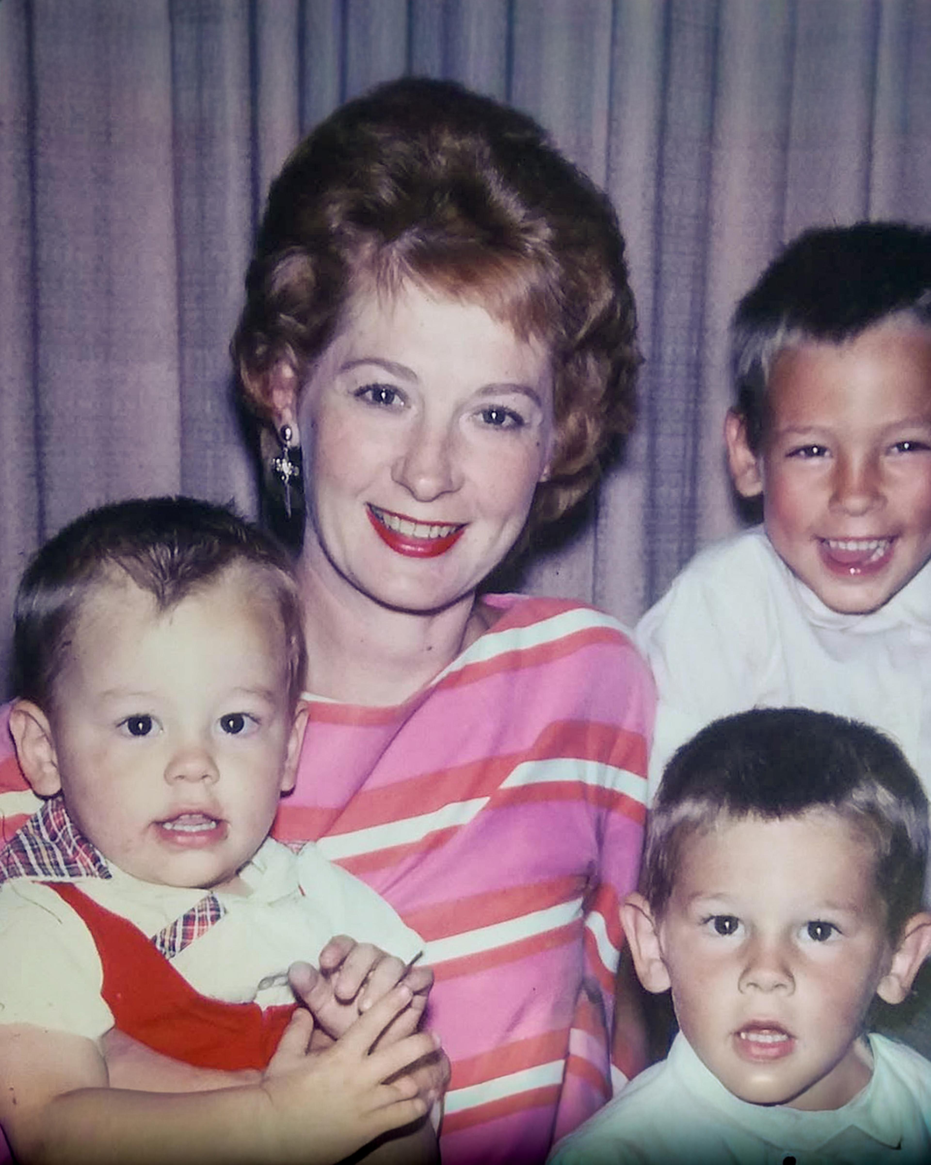 Photo of a smiling woman with three young children in front of a curtain. The woman wears a striped top.
