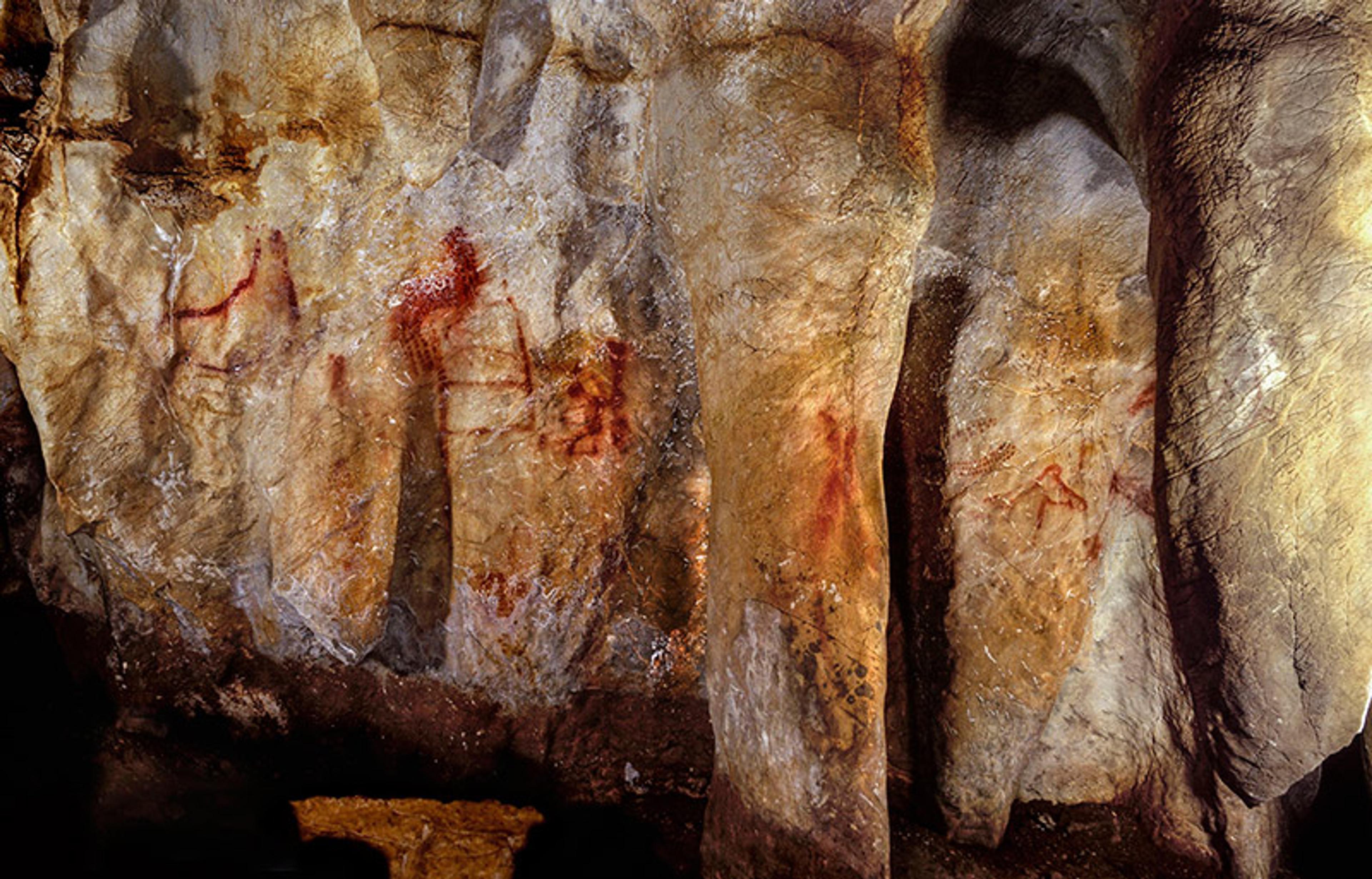 Cave painting showing red symbols on a rough stone wall.